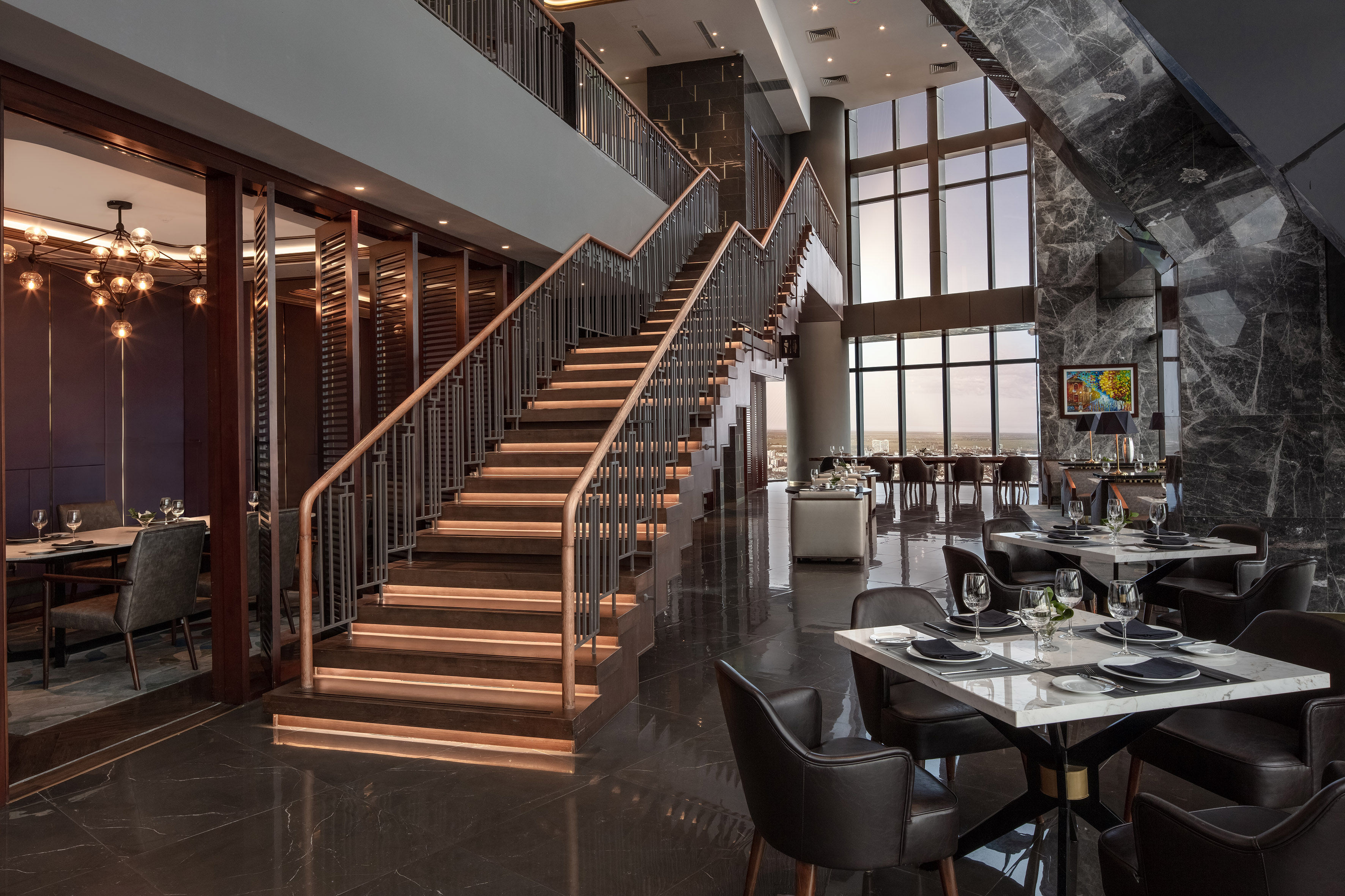 Luxury restaurant interior with grand staircase, marble, and scenic windows.