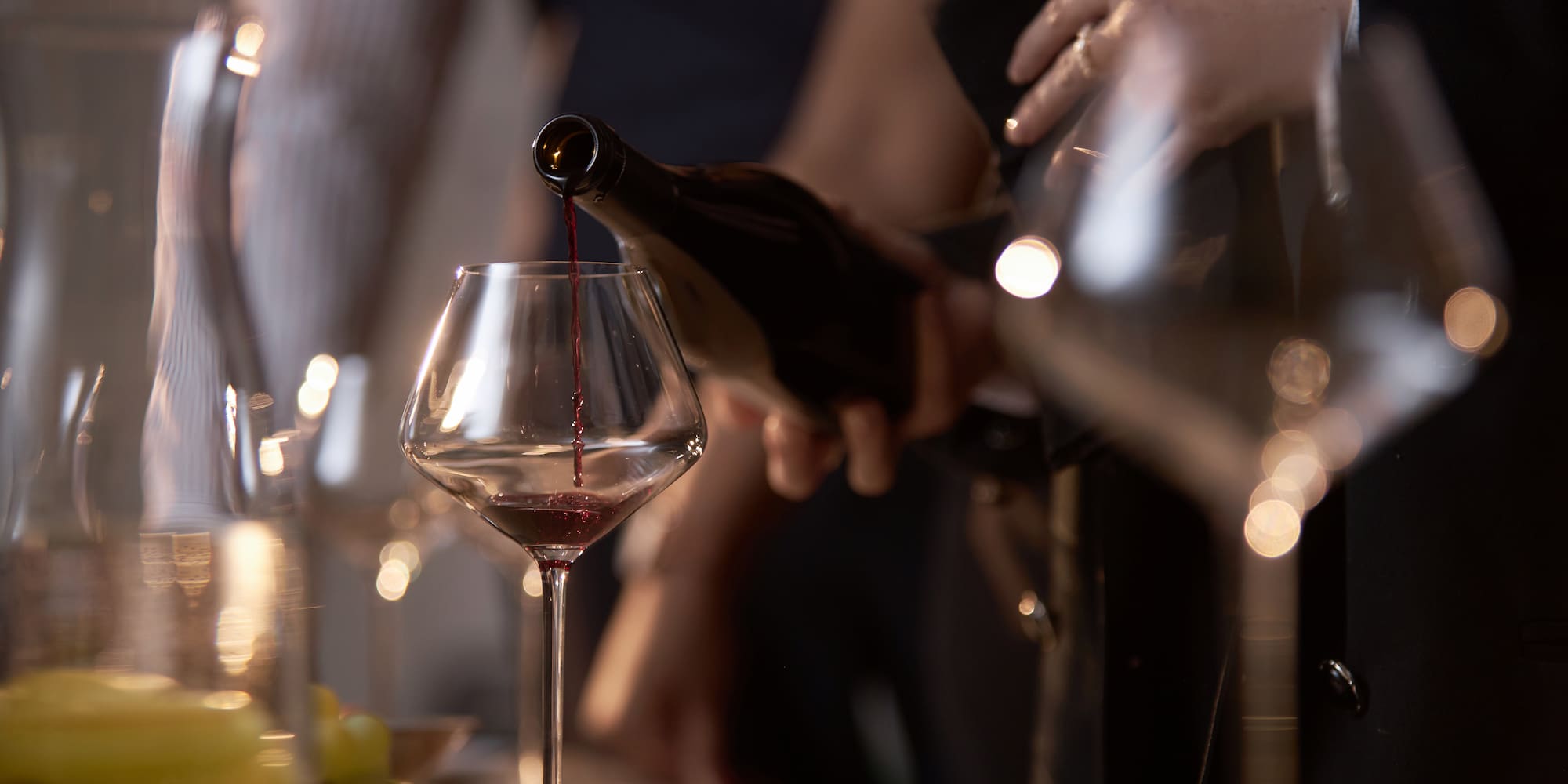 Red wine pouring from bottle into a stemmed wine glass.
