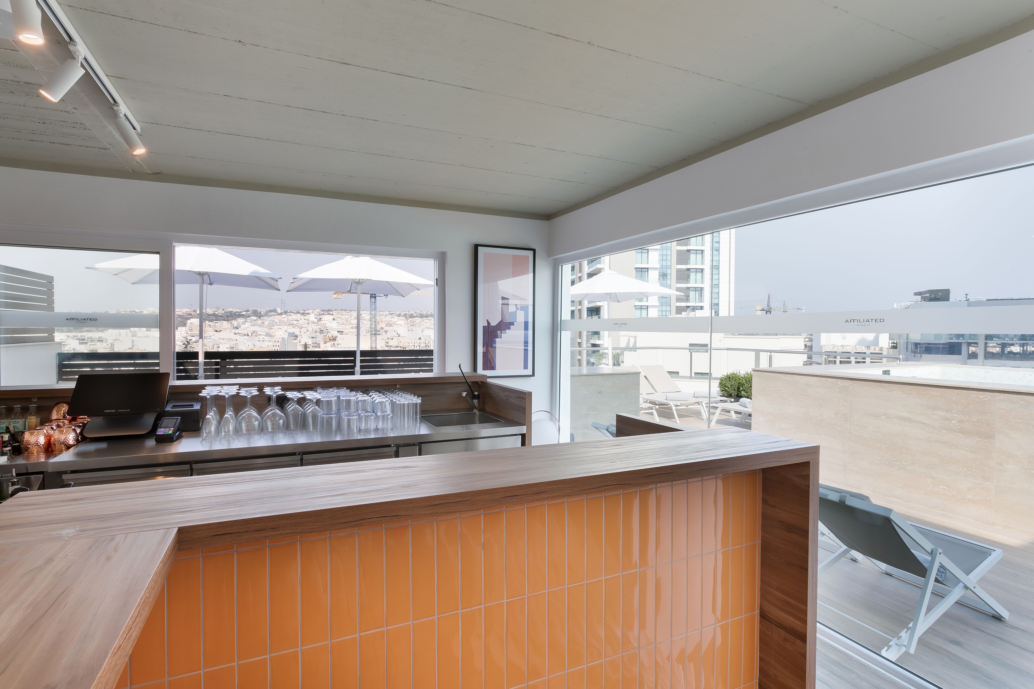 Hotel rooftop bar with orange tiled counter, city views, and outdoor lounge.