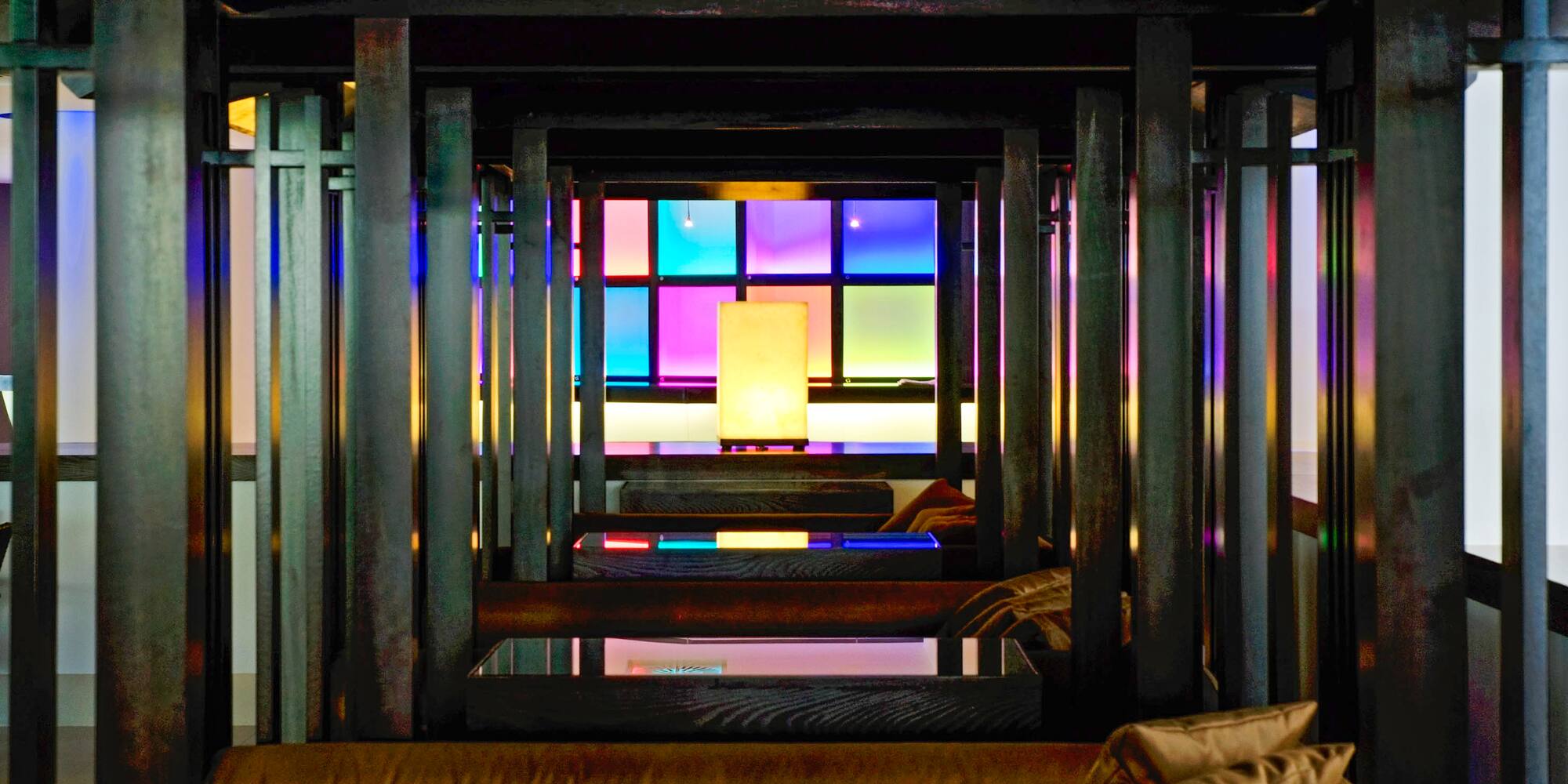 Dark modern lounge with wooden beams, colorful glowing grid wall, and central lamp.