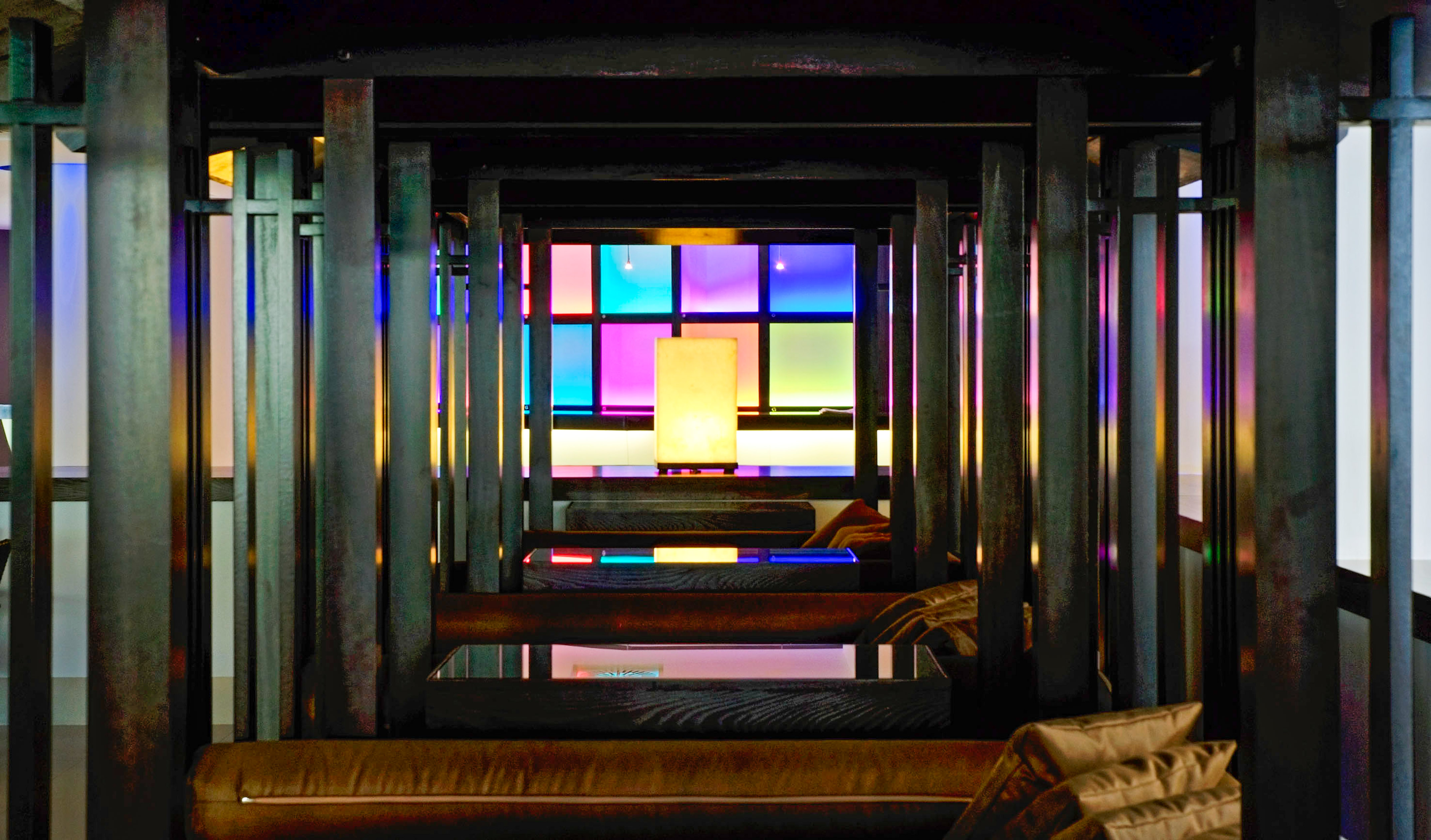 Dark modern lounge with wooden beams, colorful glowing grid wall, and central lamp.