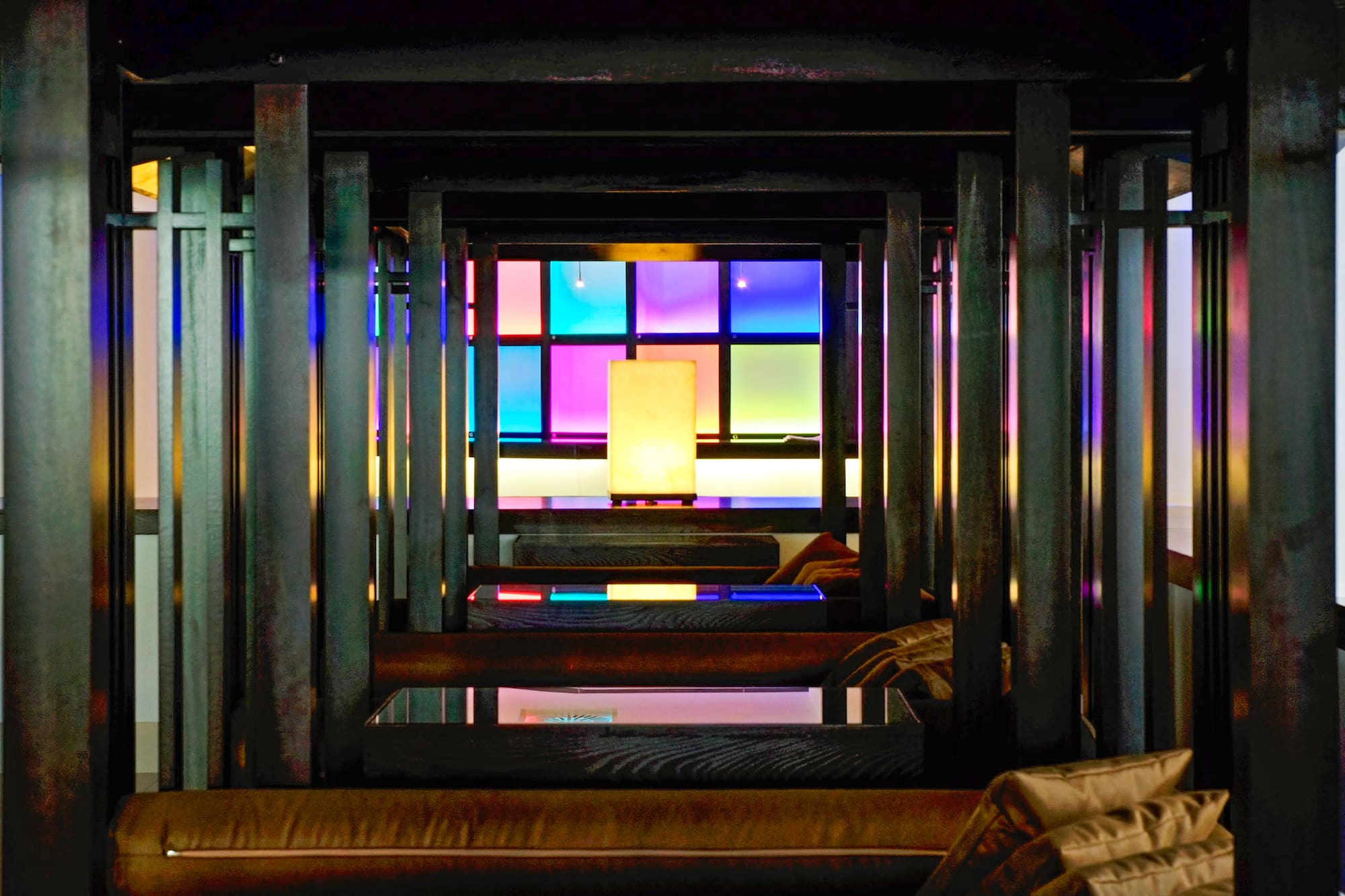 Dark modern lounge with wooden beams, colorful glowing grid wall, and central lamp.