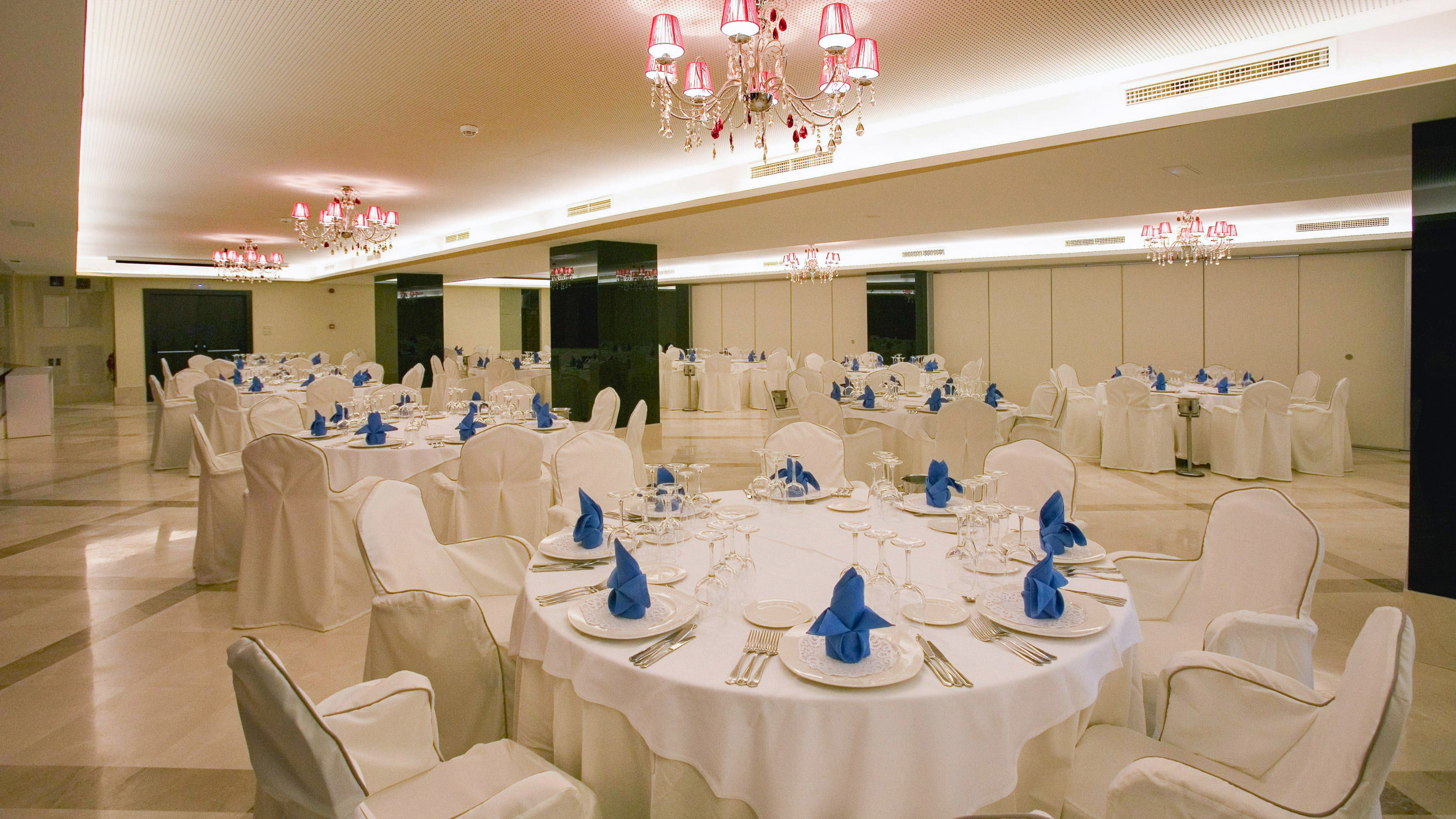 Banquet hall with white draped tables, blue napkins, and pink chandeliers.