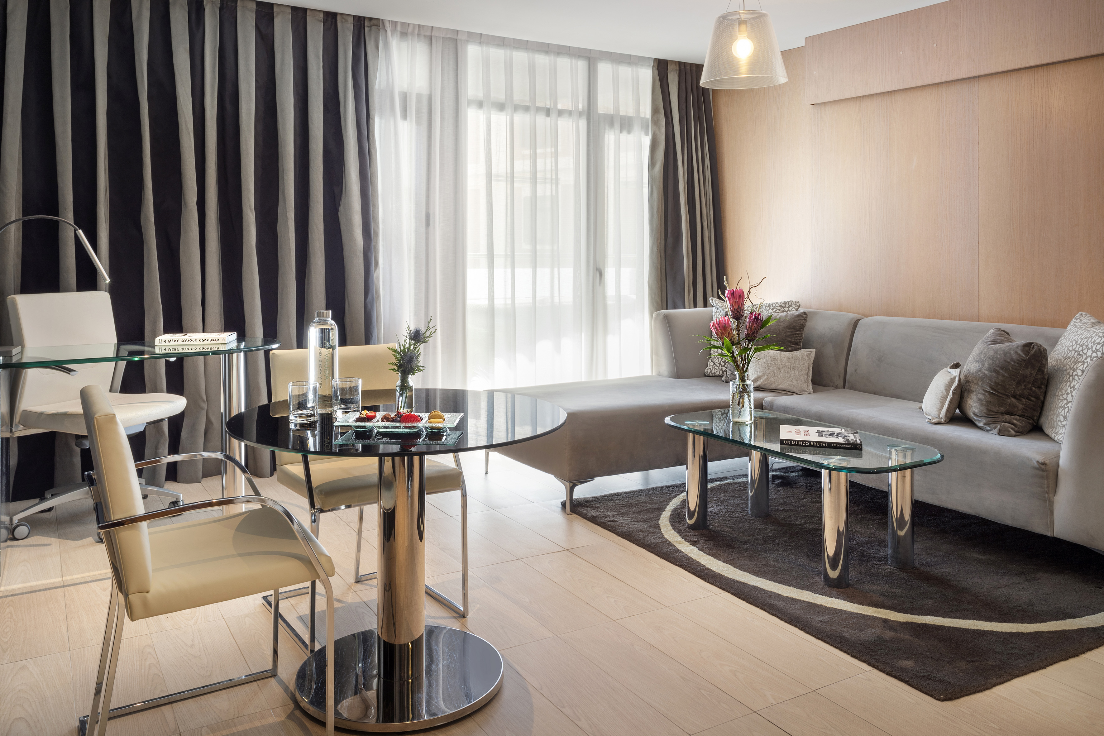 Contemporary suite: gray sofa, glass tables, wood floor, dark striped curtains.