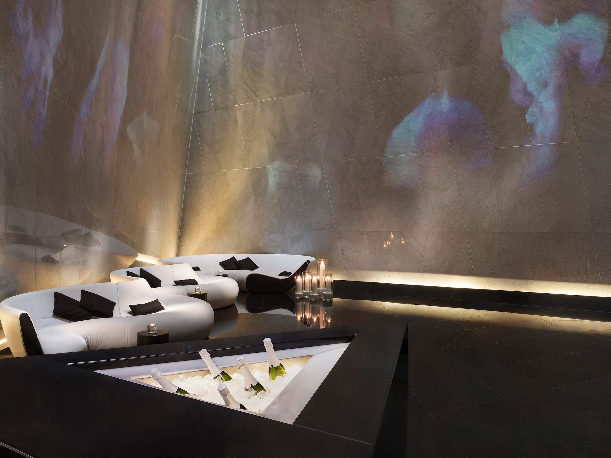 Luxury lounge bar with white sofas, champagne cooler, and ambient projections.