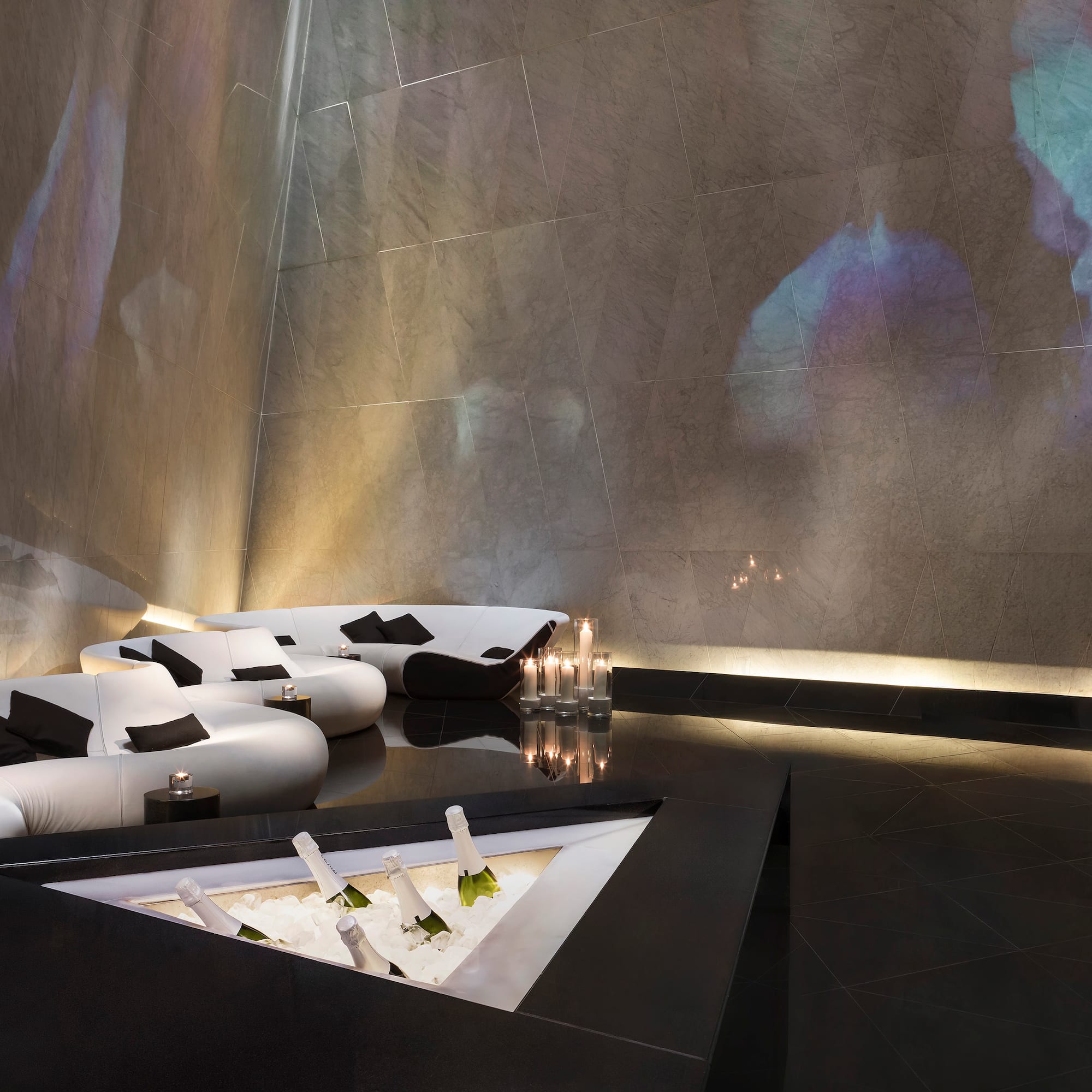 Sleek modern lounge: white sofas, champagne cooler, abstract wall projections.