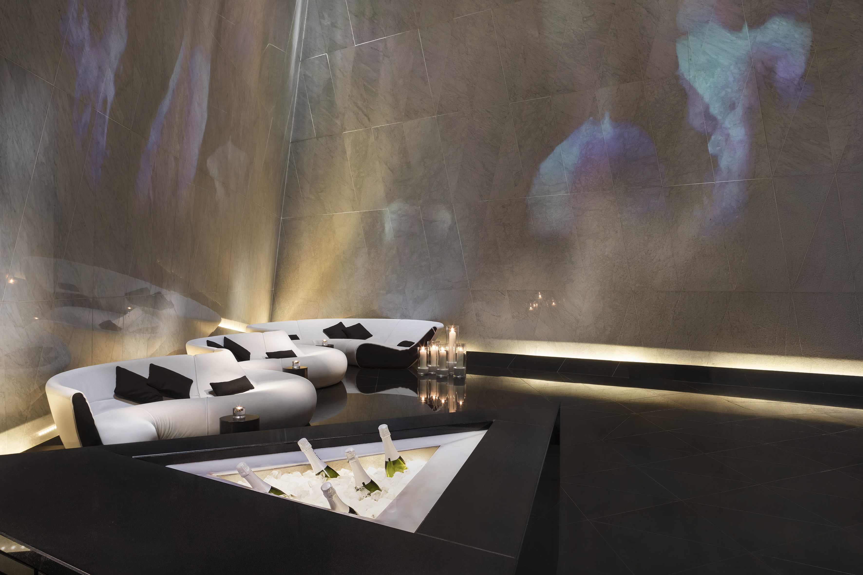 Luxury lounge bar with white sofas, champagne cooler, and ambient projections.