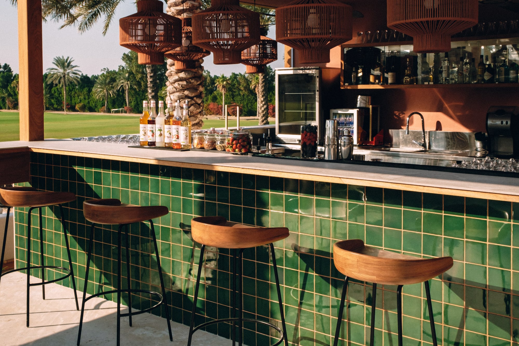 Resort outdoor bar with green tiles, wooden stools, and tropical golf course view.