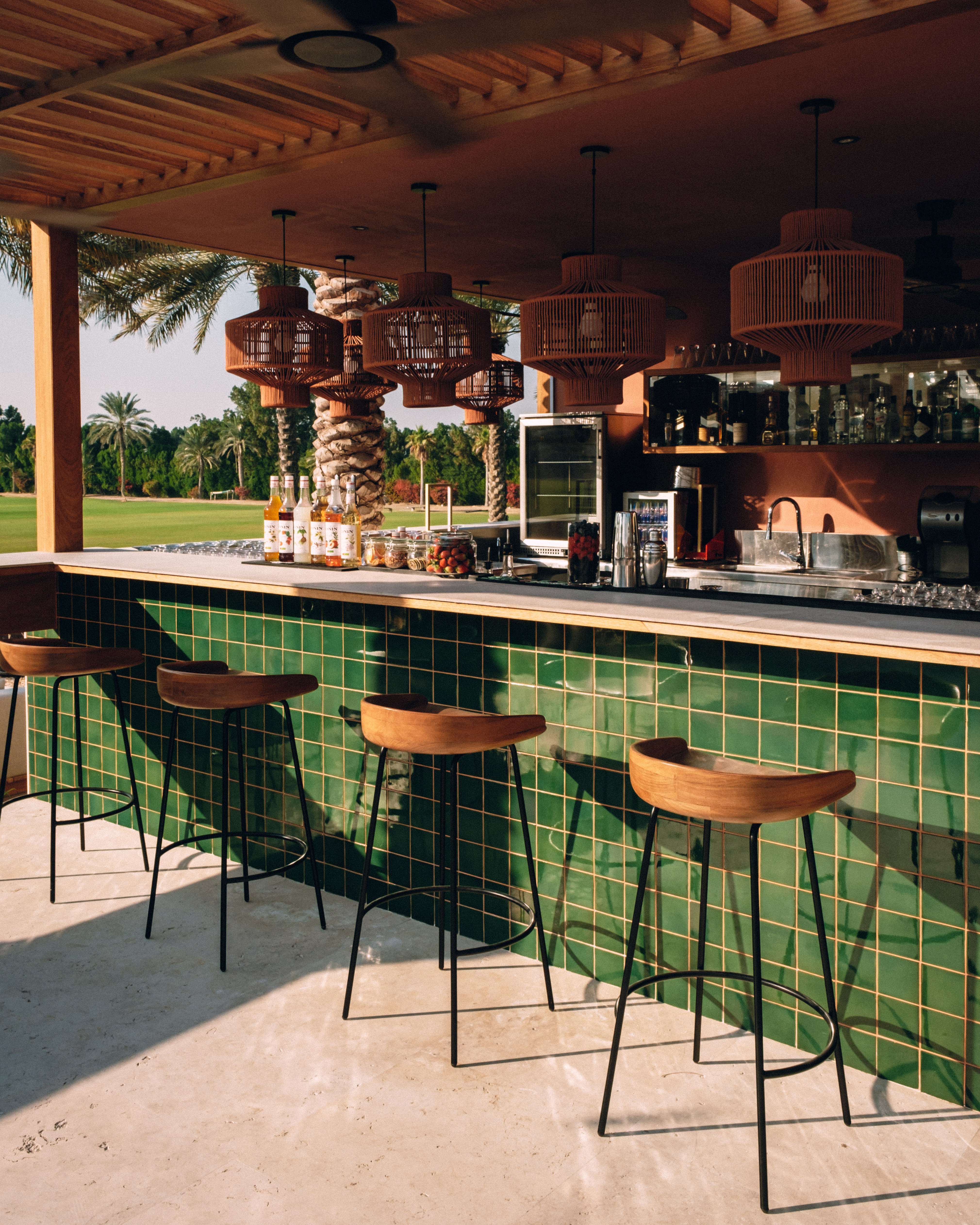 Resort outdoor bar with green tiles, wooden stools, and tropical golf course view.