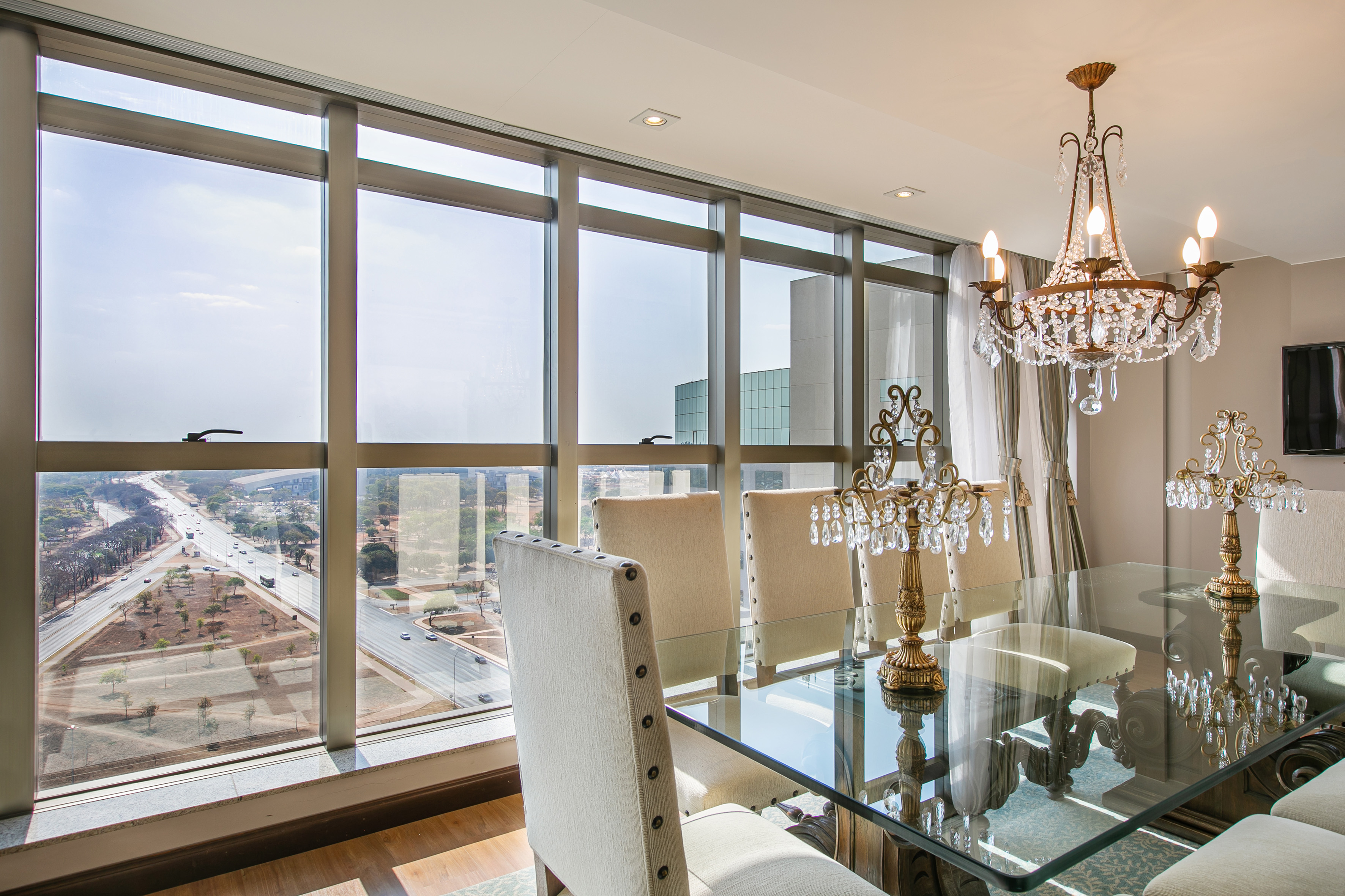 Elegant dining room with glass table, crystal chandeliers, and expansive city view.