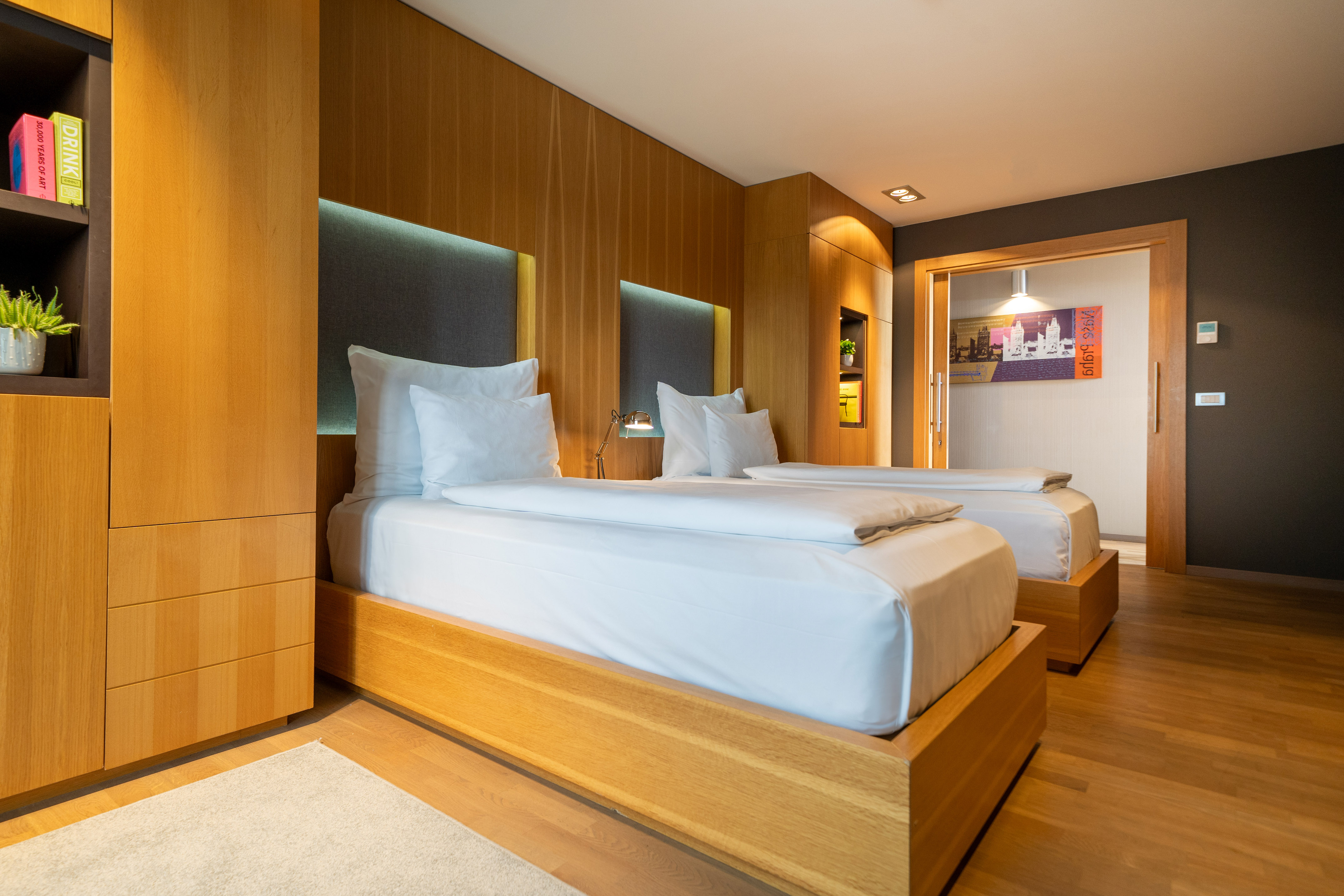 Modern hotel room with two twin beds, wooden walls, and backlit headboards.