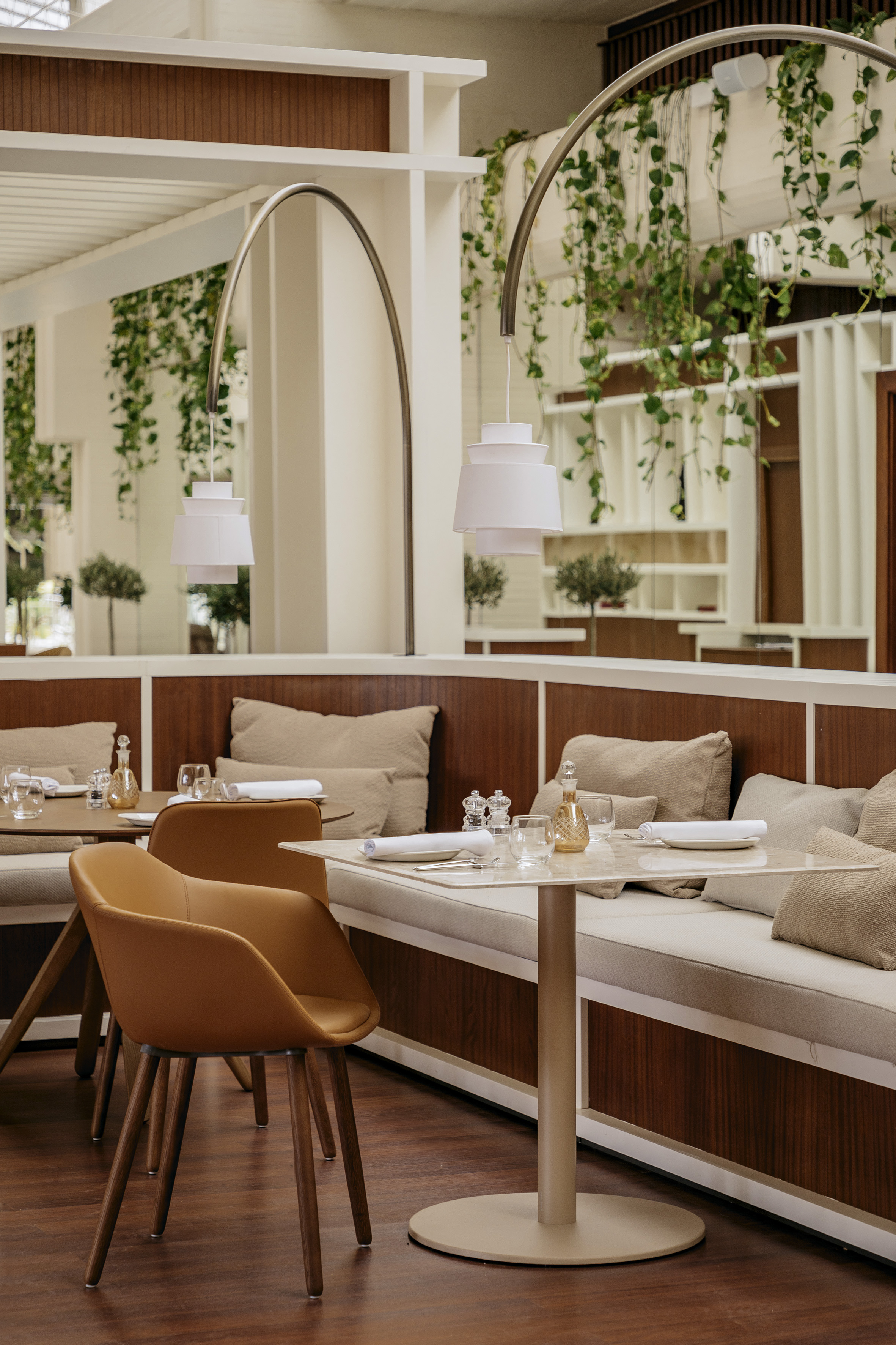 Stylish restaurant interior with set tables, booth seating, and hanging greenery.