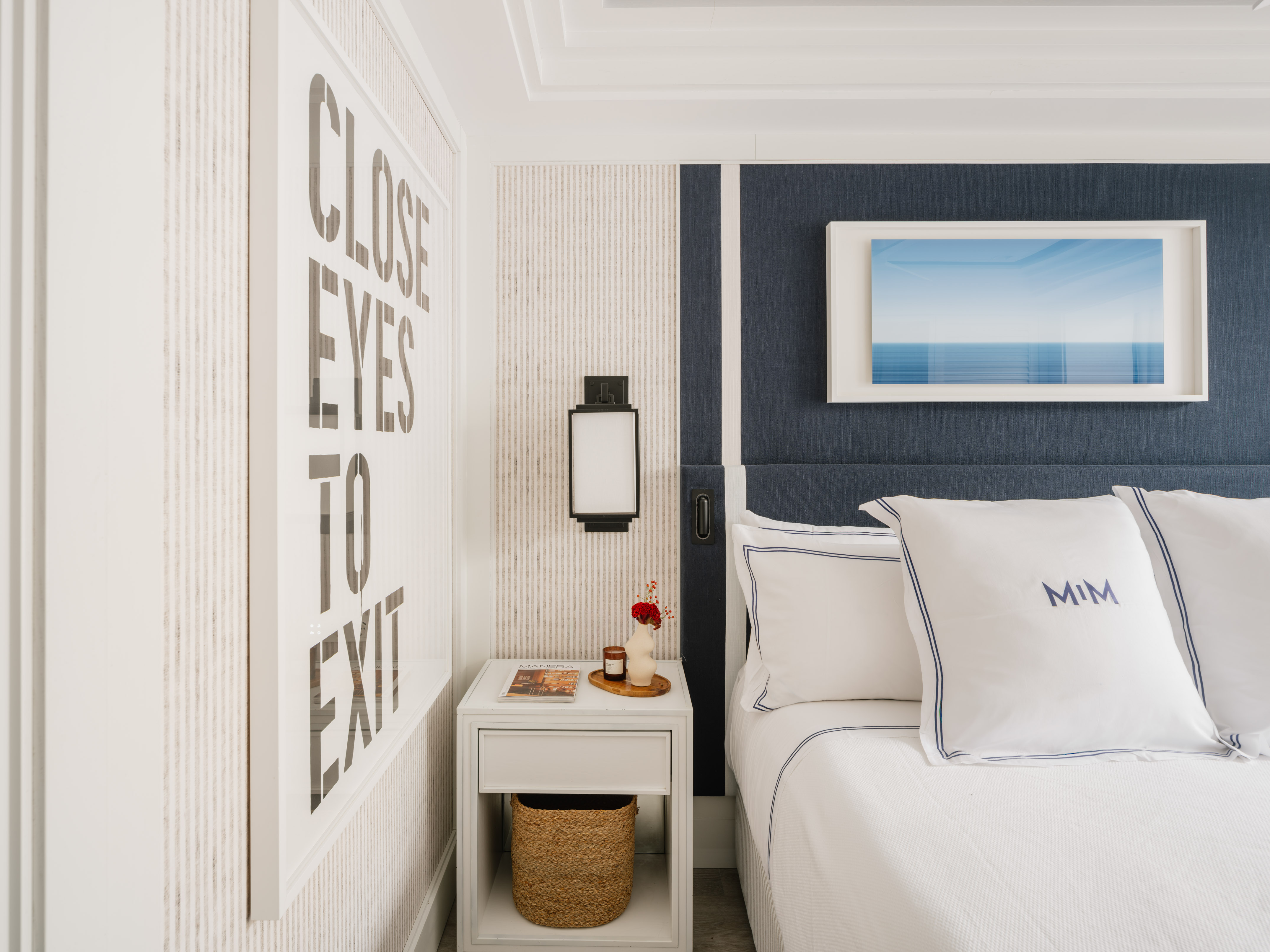 Modern bedroom with white bed, navy headboard, nightstand, and wall art.