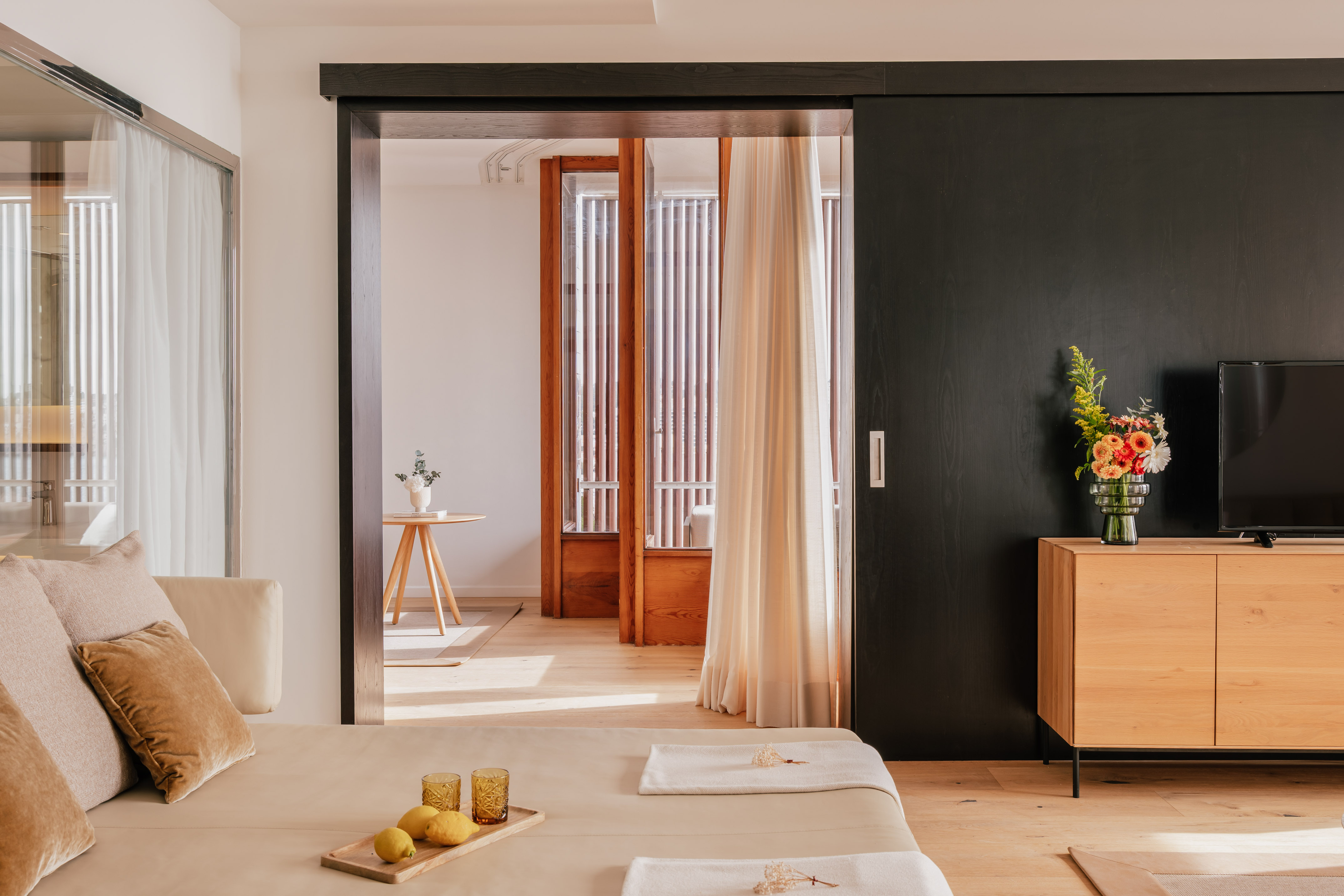 Modern hotel suite with daybed, black sliding door, and wood cabinet.