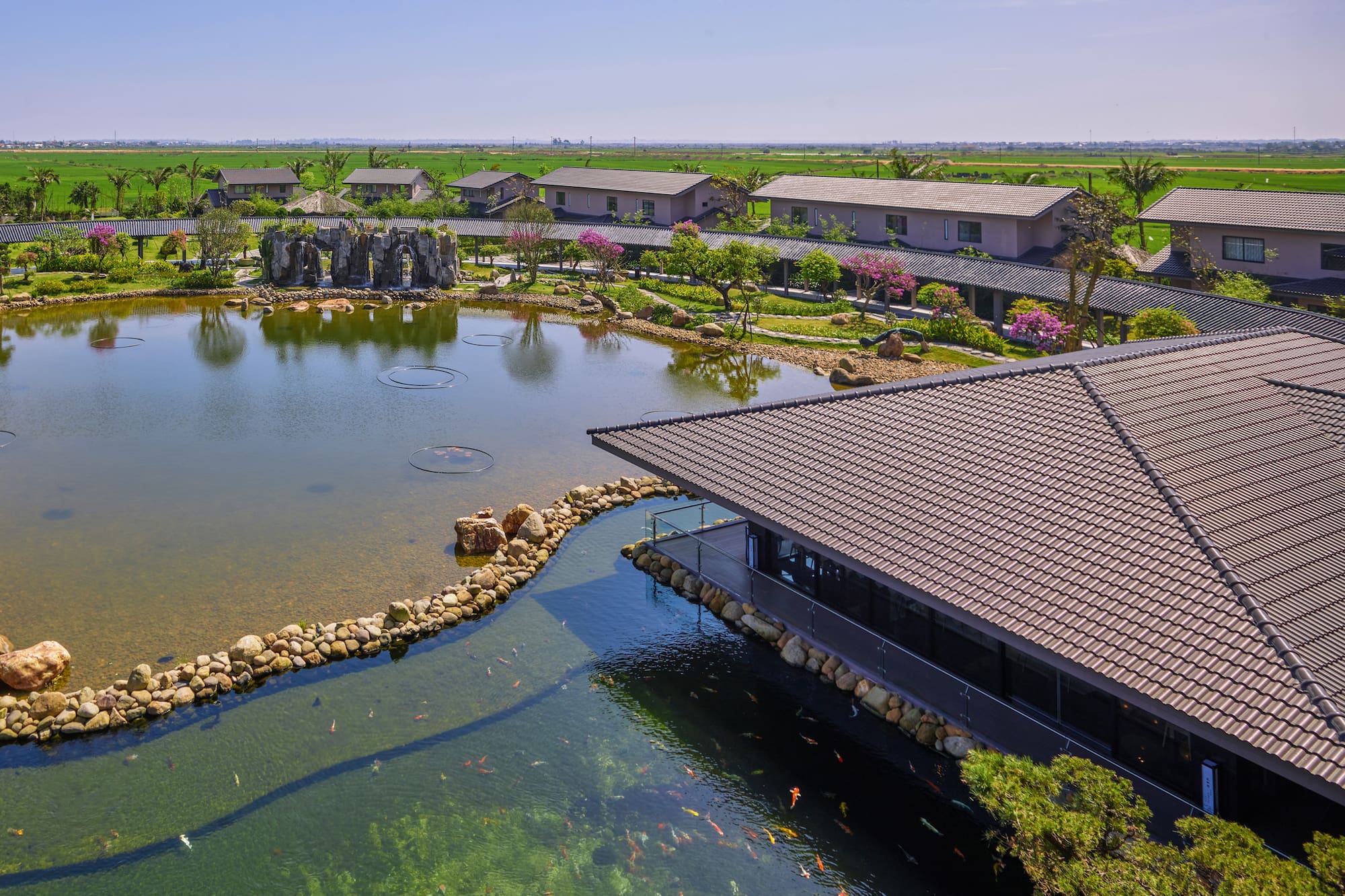 Aerial view of scenic koi pond, traditional buildings, and lush green fields.