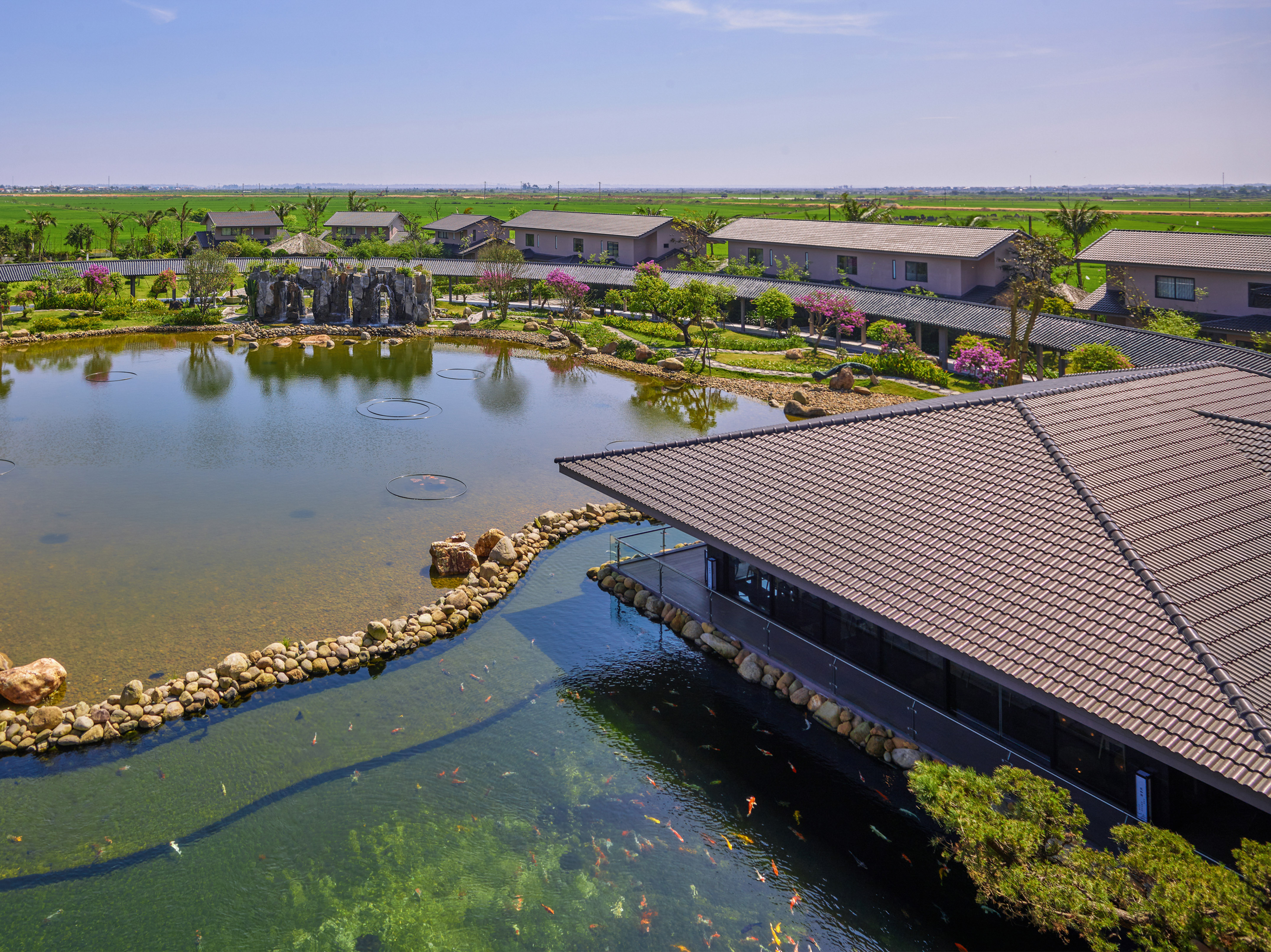 Aerial view of scenic koi pond, traditional buildings, and lush green fields.