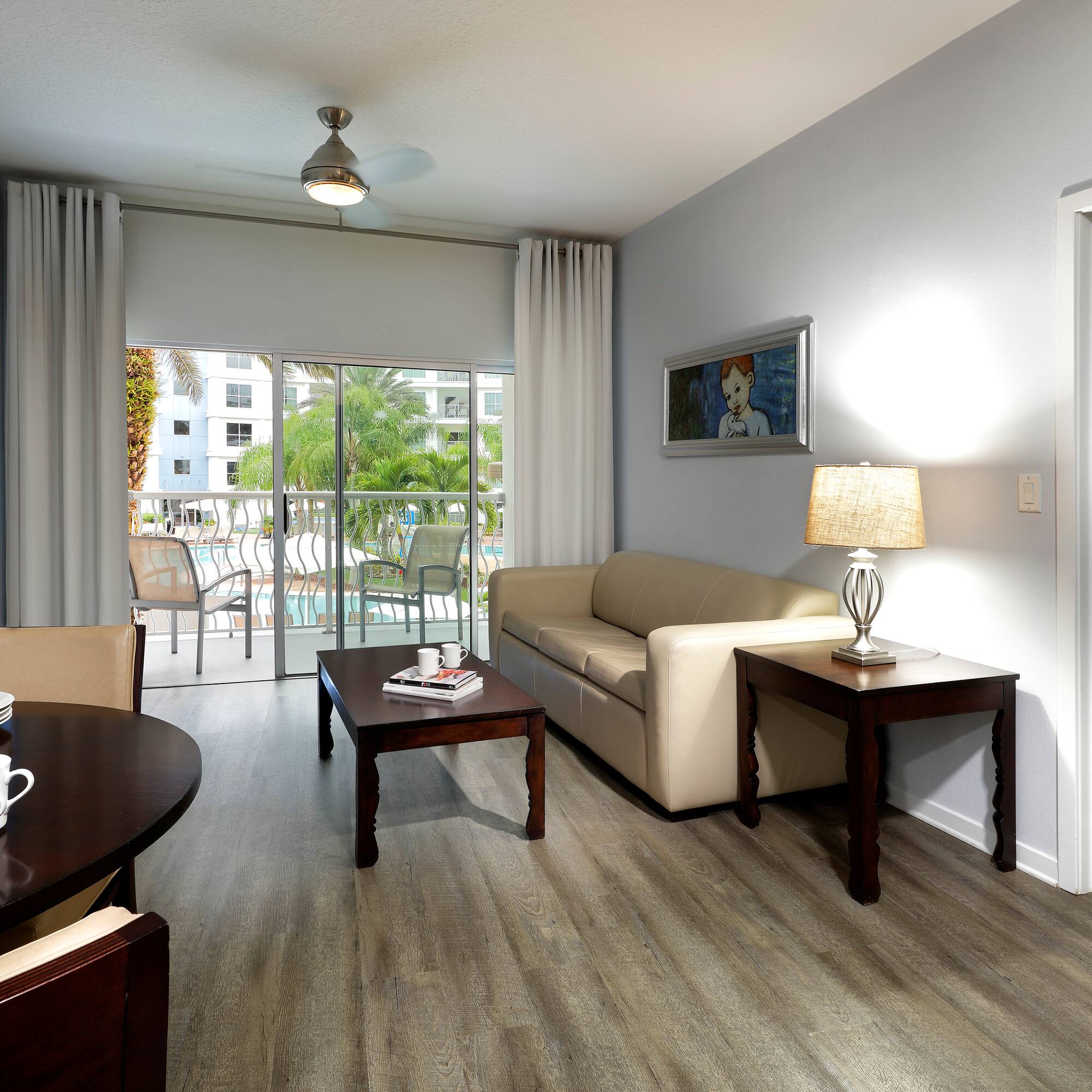 Hotel suite living room with dining, sofa, TV, and pool view balcony.