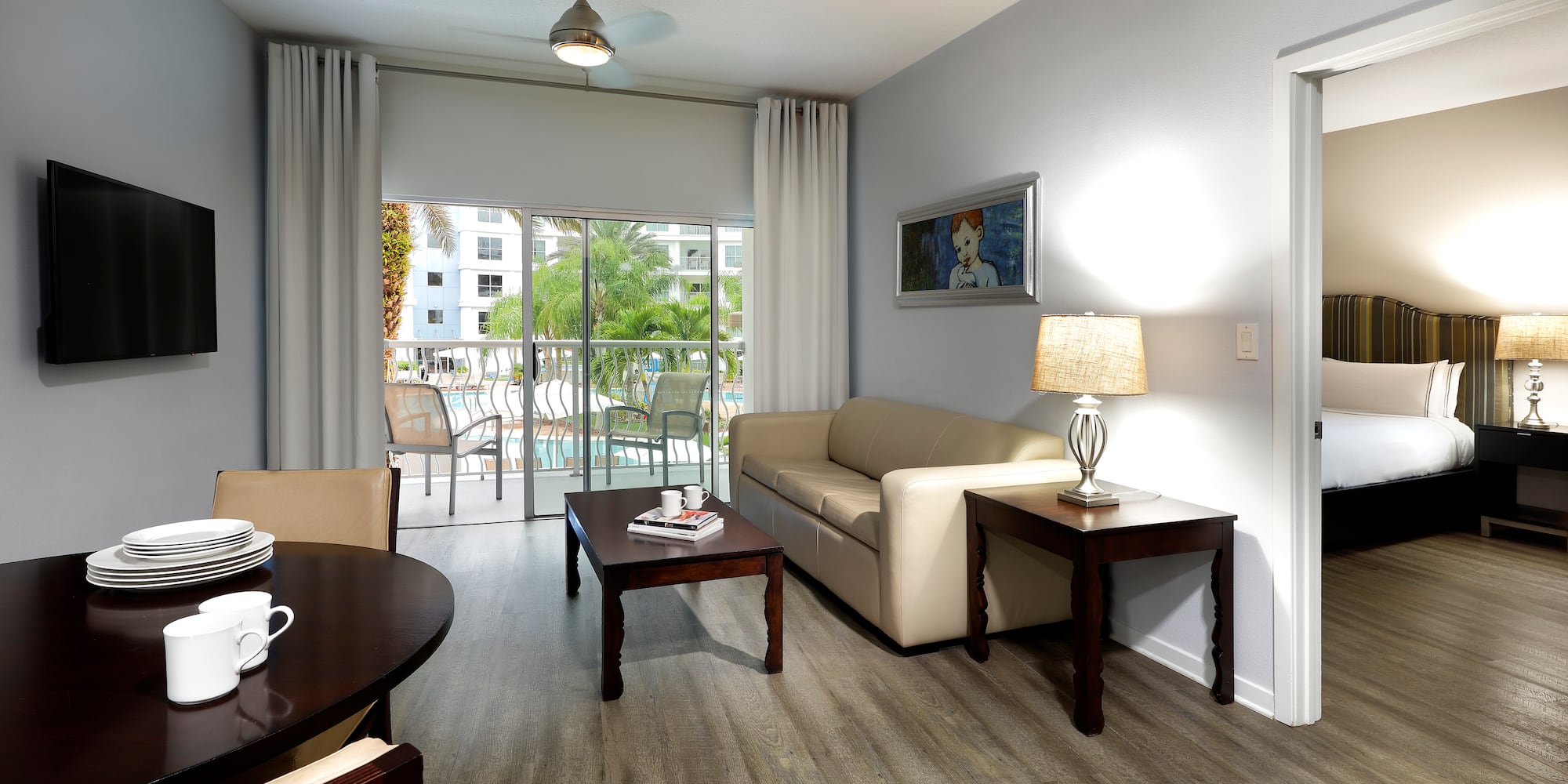 Hotel suite living room with dining, sofa, TV, and pool view balcony.