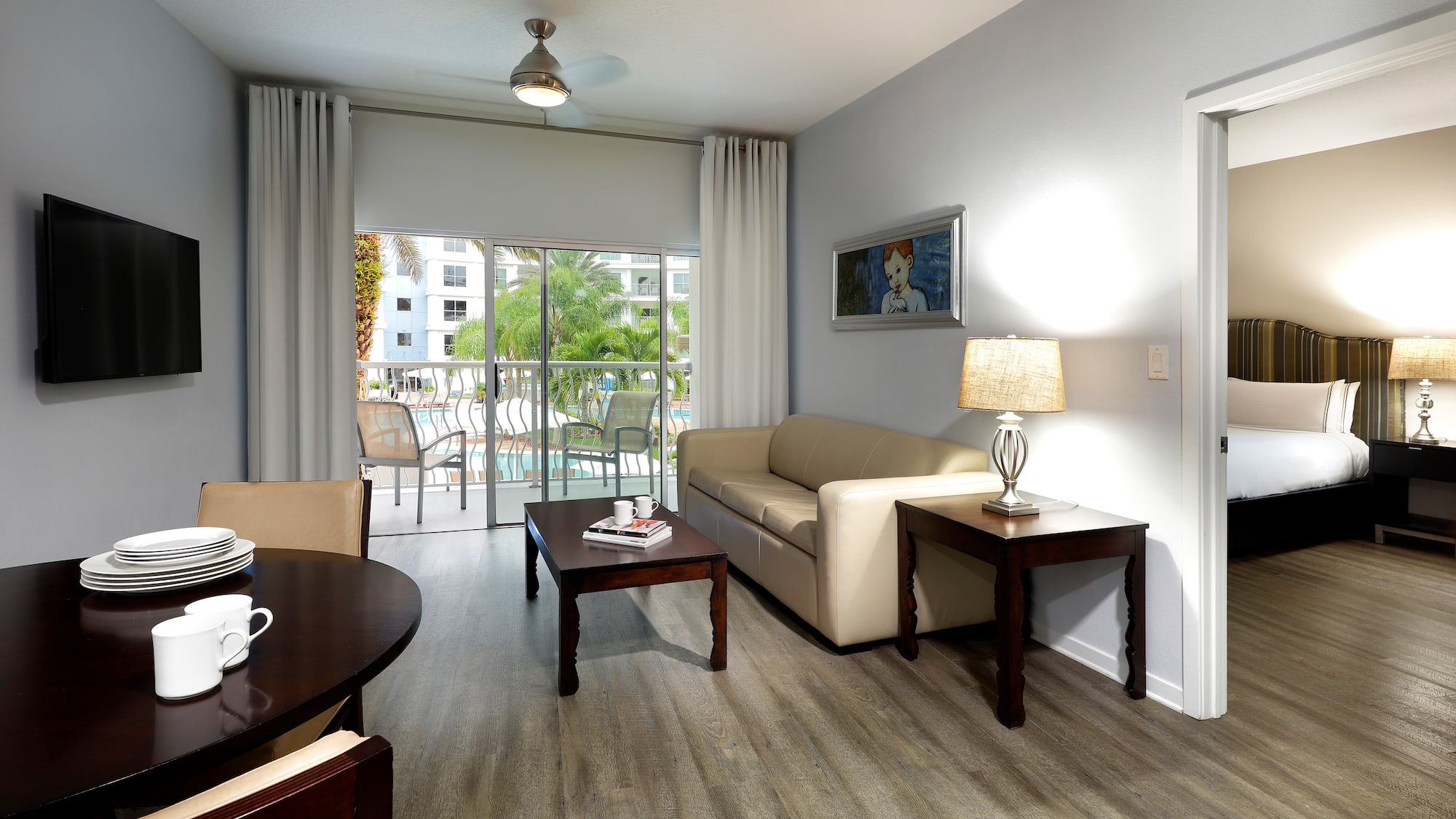 Hotel suite living room with dining, sofa, TV, and pool view balcony.