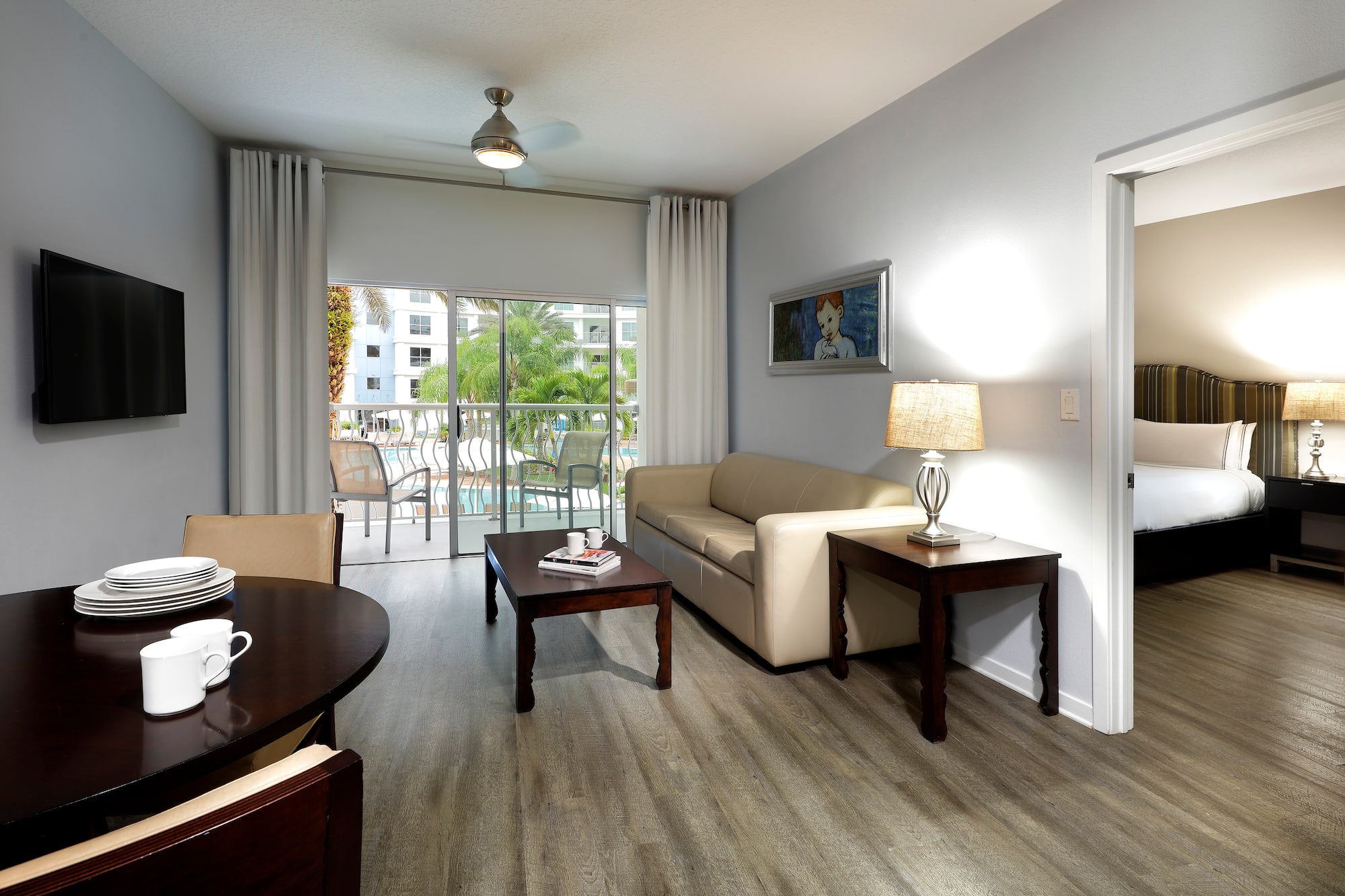 Hotel suite living room with dining, sofa, TV, and pool view balcony.