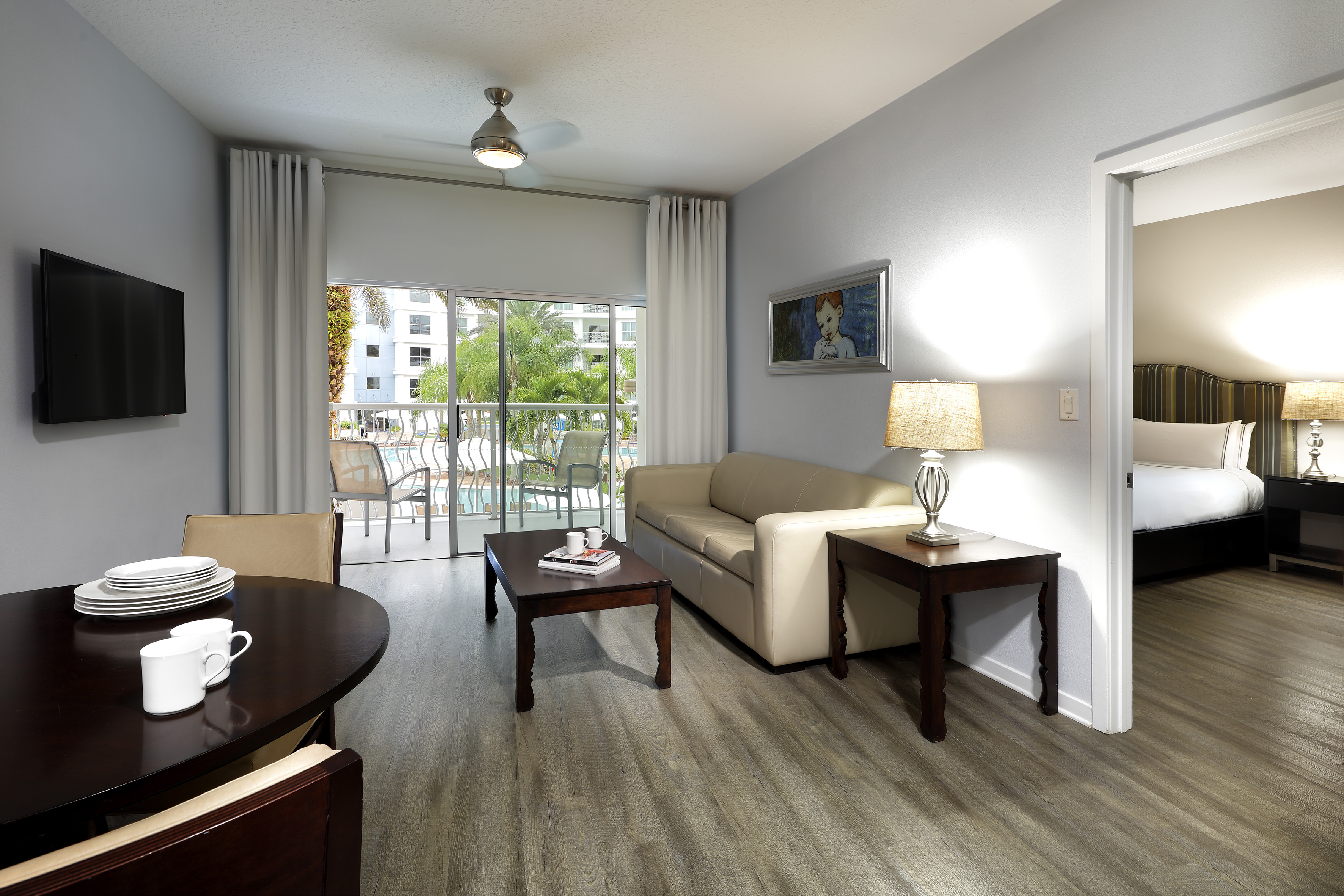 Hotel suite living room with dining, sofa, TV, and pool view balcony.