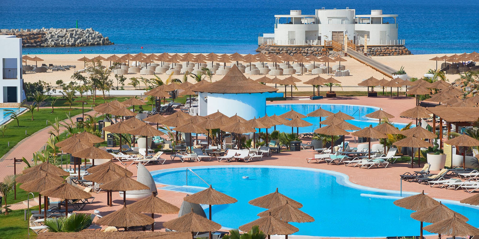 a pool with umbrellas and chairs on a beach