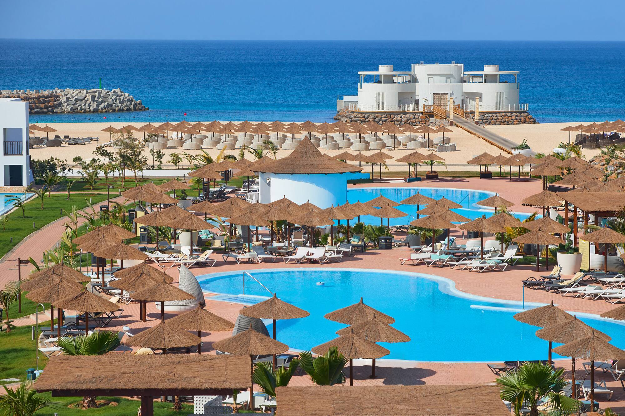 a pool with umbrellas and chairs on a beach
