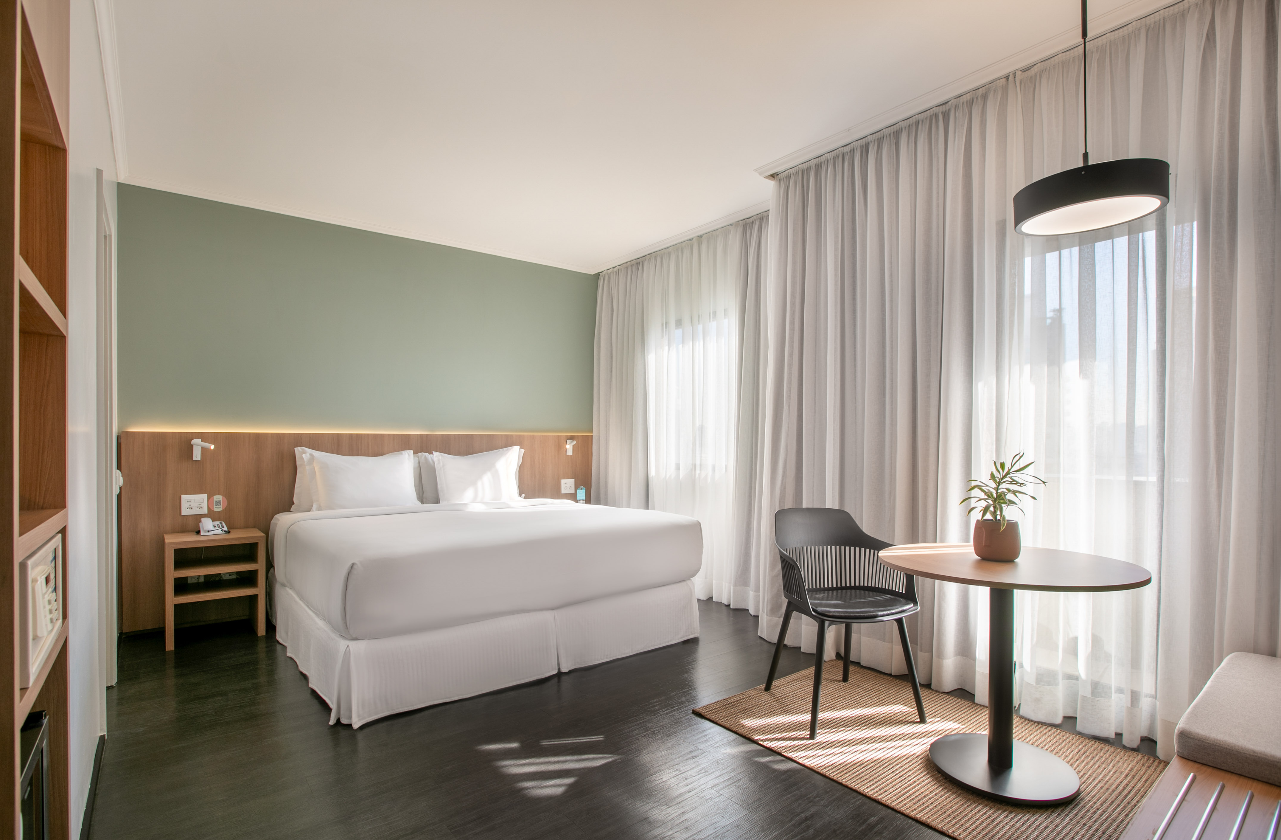 Modern hotel room with king bed, green wall, wood floor, and cozy seating area.