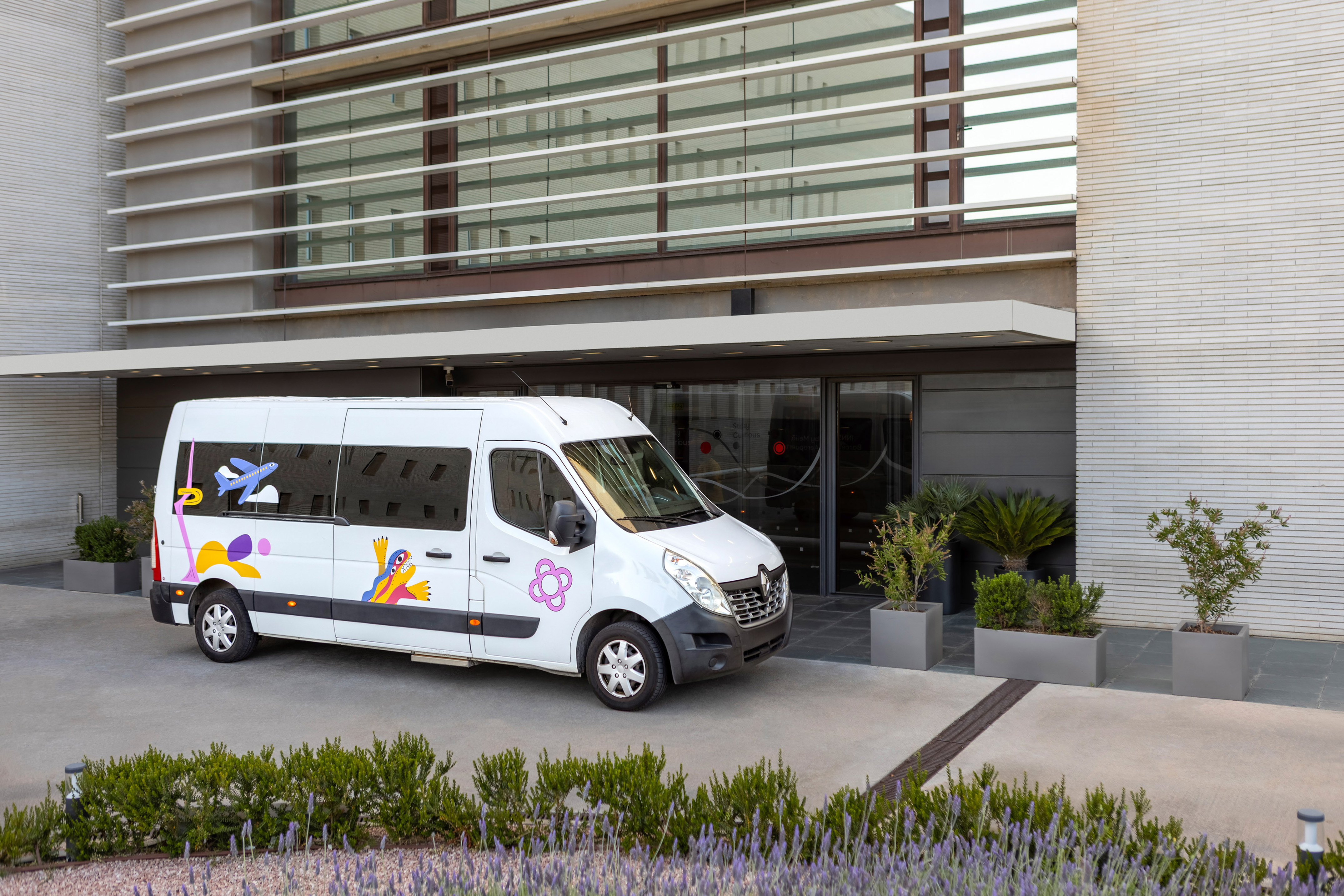 White airport shuttle van with colorful decals outside modern building.