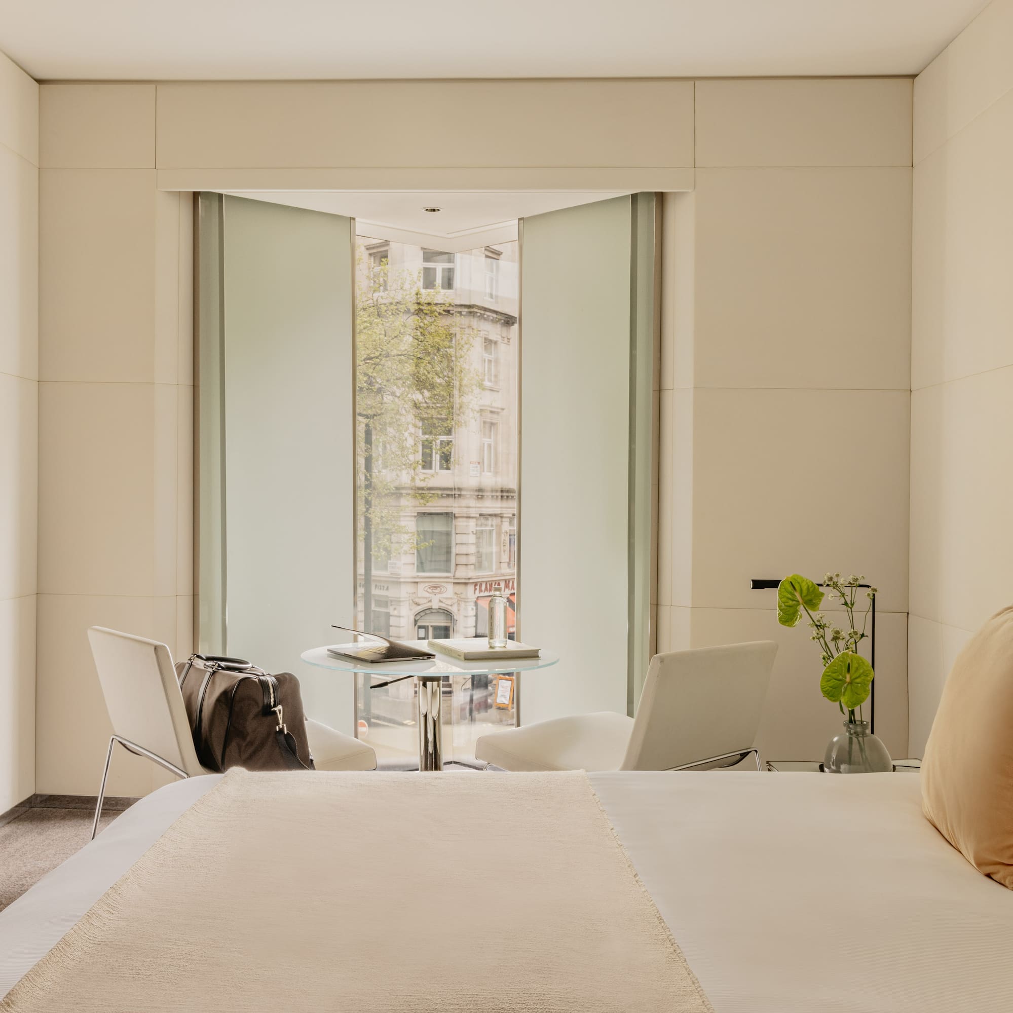 Deluxe King room at ME London Hotel with a comfortable bed, a chair with a table, and big window with city views.