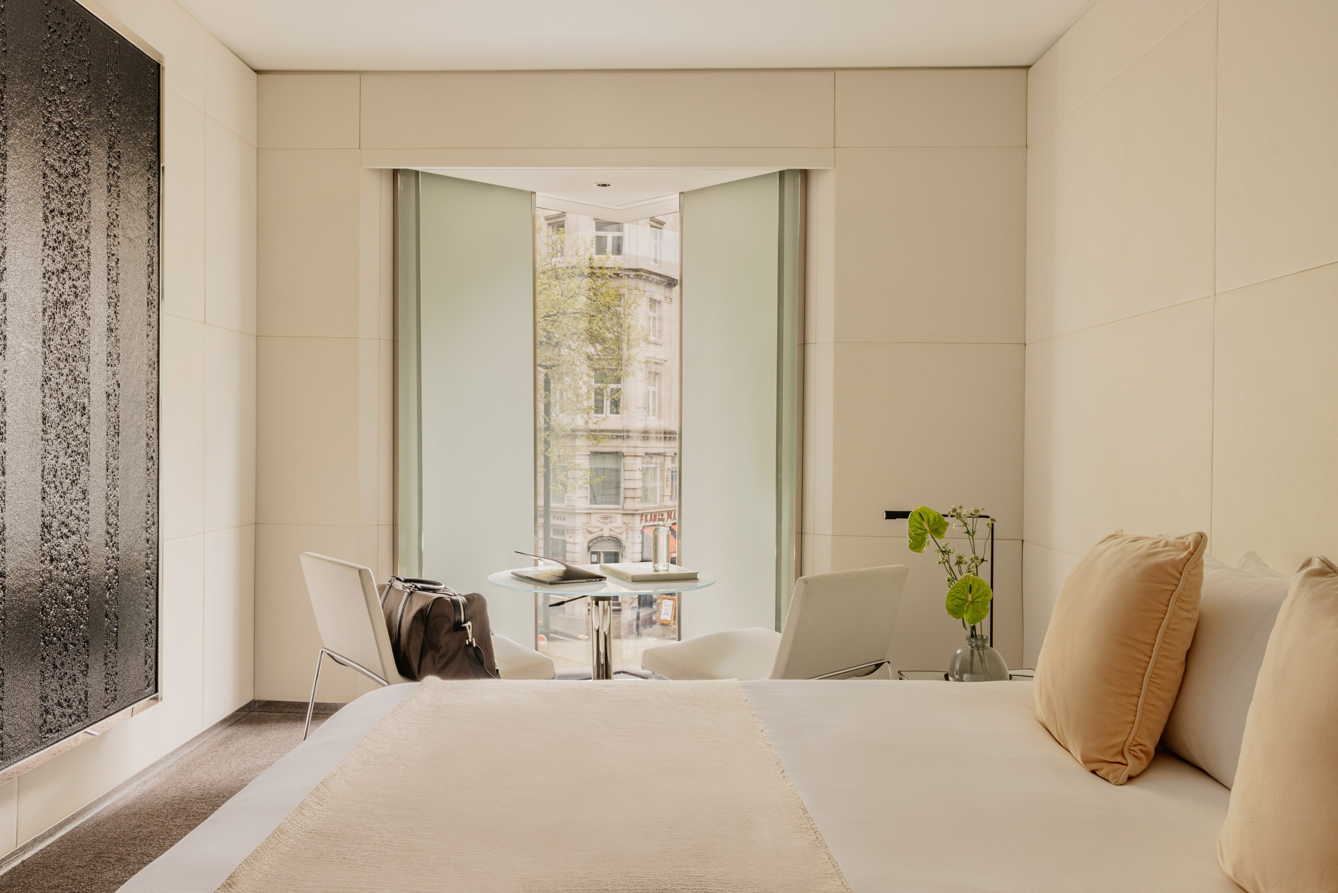 Modern hotel room with city view, crisp white bed, and minimalist design.