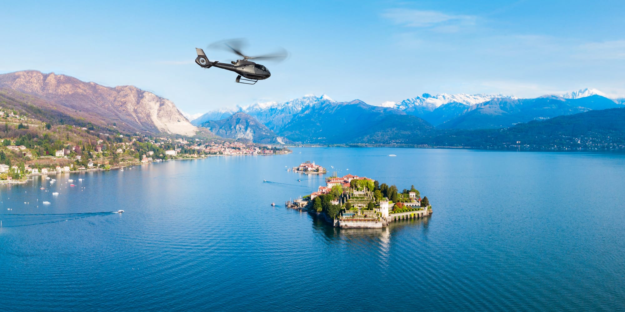 Helicopter above Isola Bella, Lake Maggiore, with snow-capped mountains.