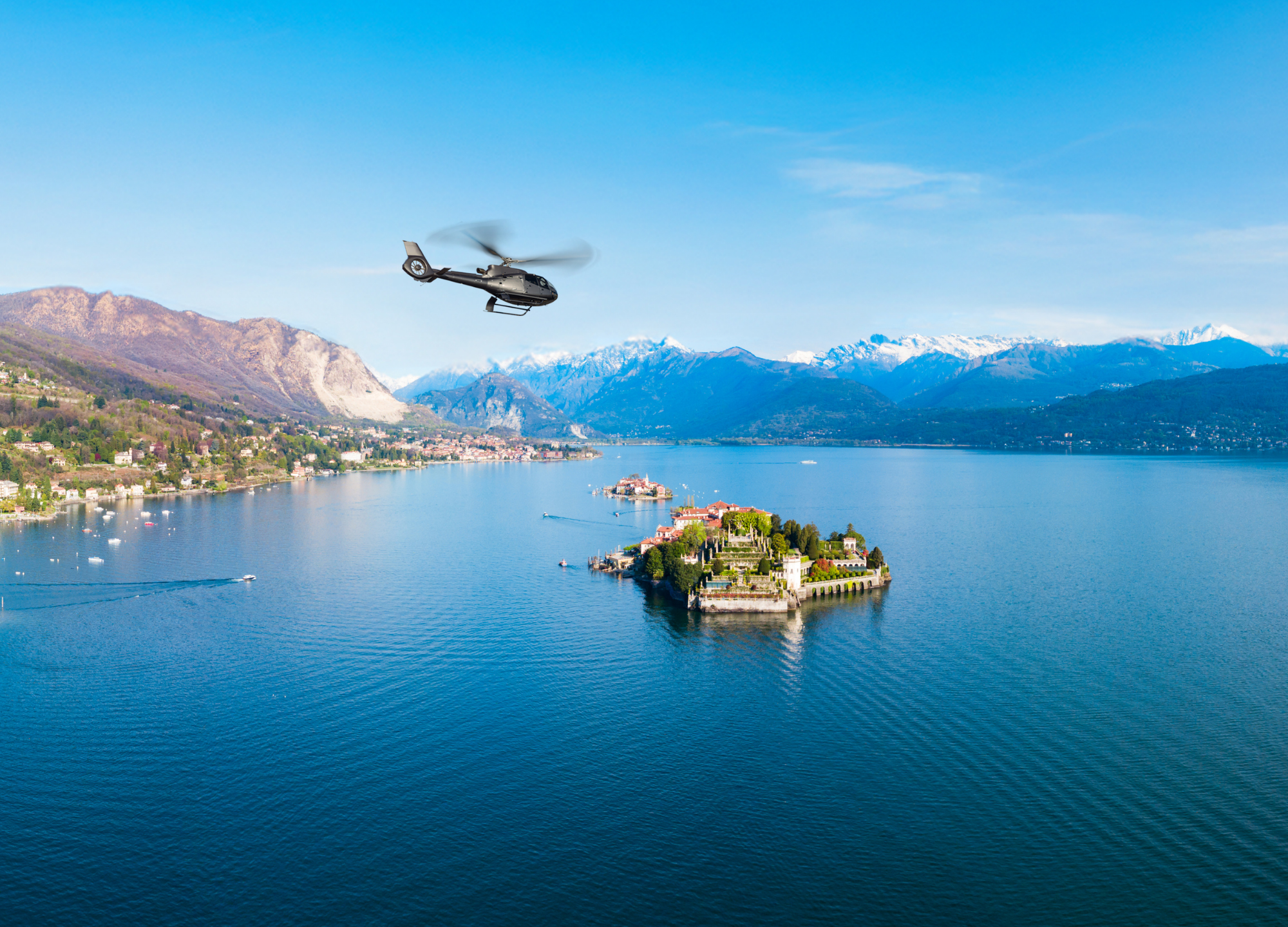 Helicopter above Isola Bella, Lake Maggiore, with snow-capped mountains.