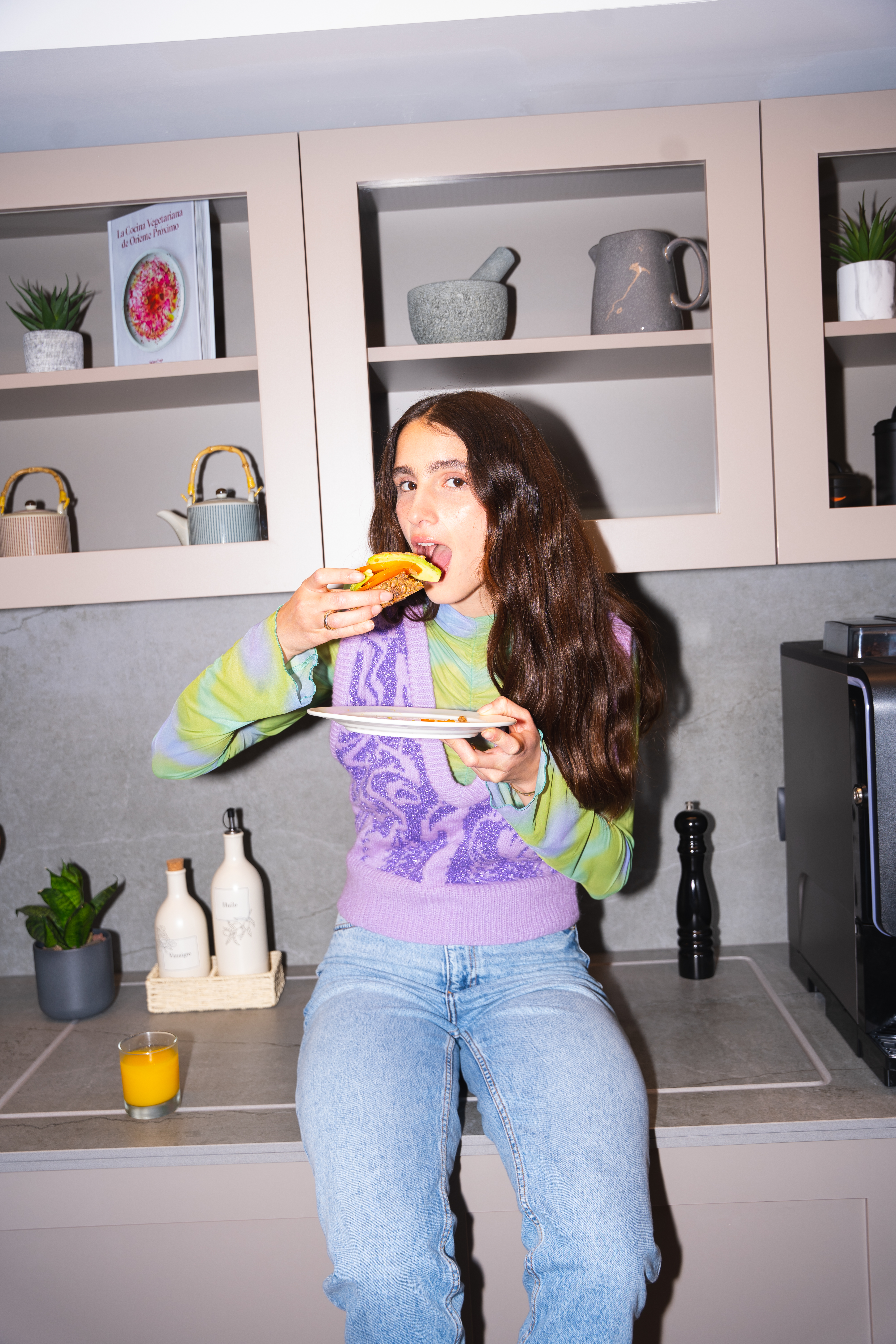 Woman eating a vegetable sandwich on a kitchen counter in a modern home.