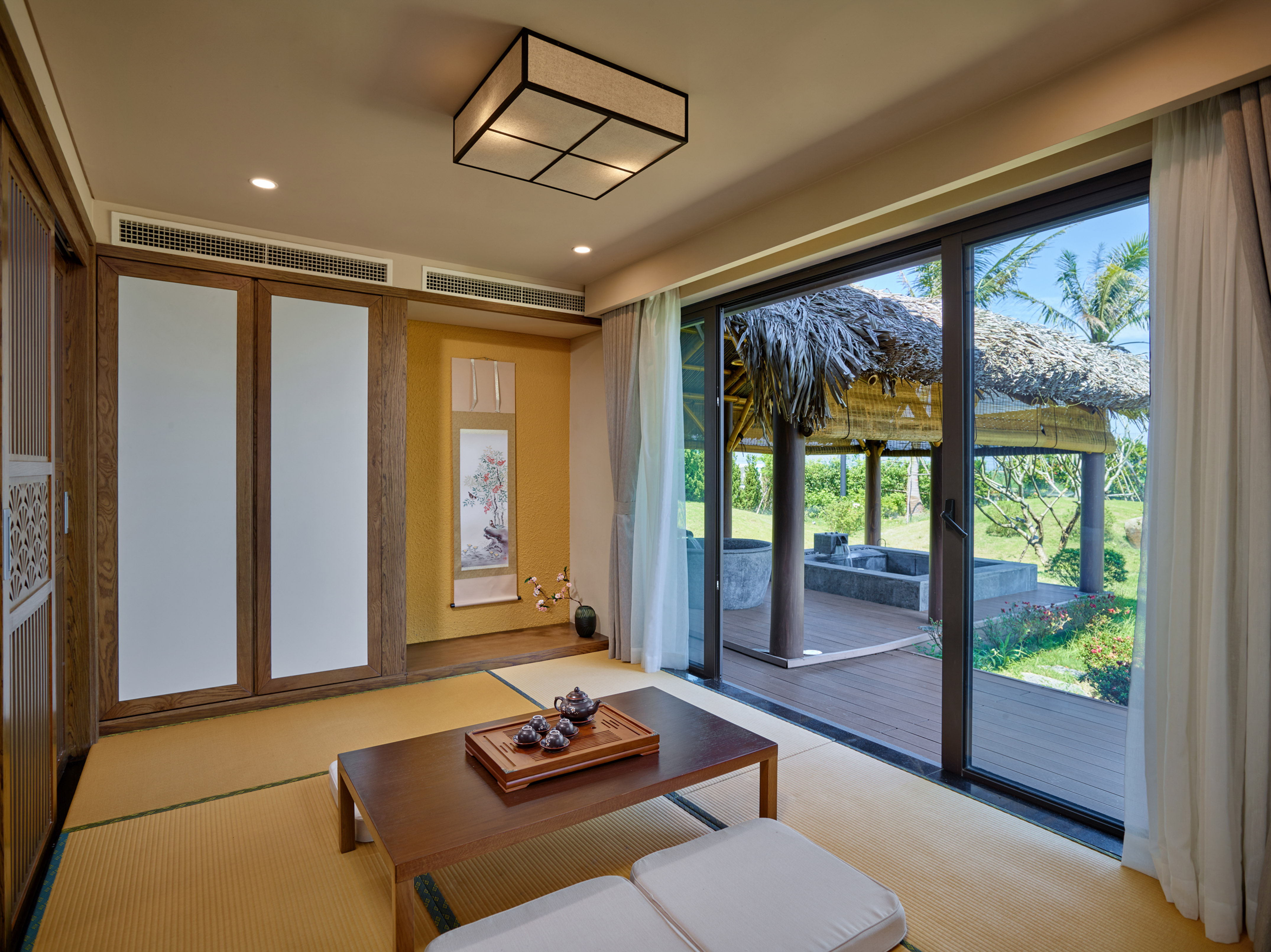 Japanese tatami room with tea set, sliding doors, and tropical patio view.
