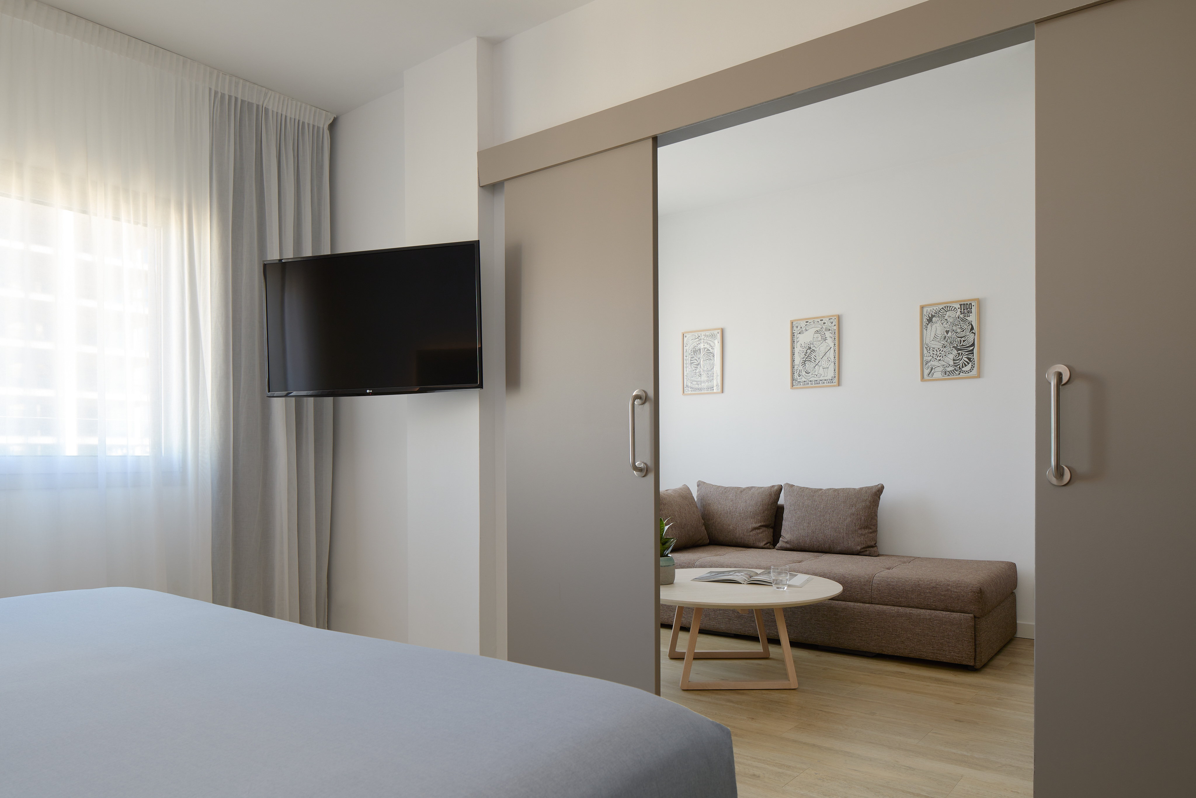 Modern hotel room with TV, grey sliding door to living area with sofa.
