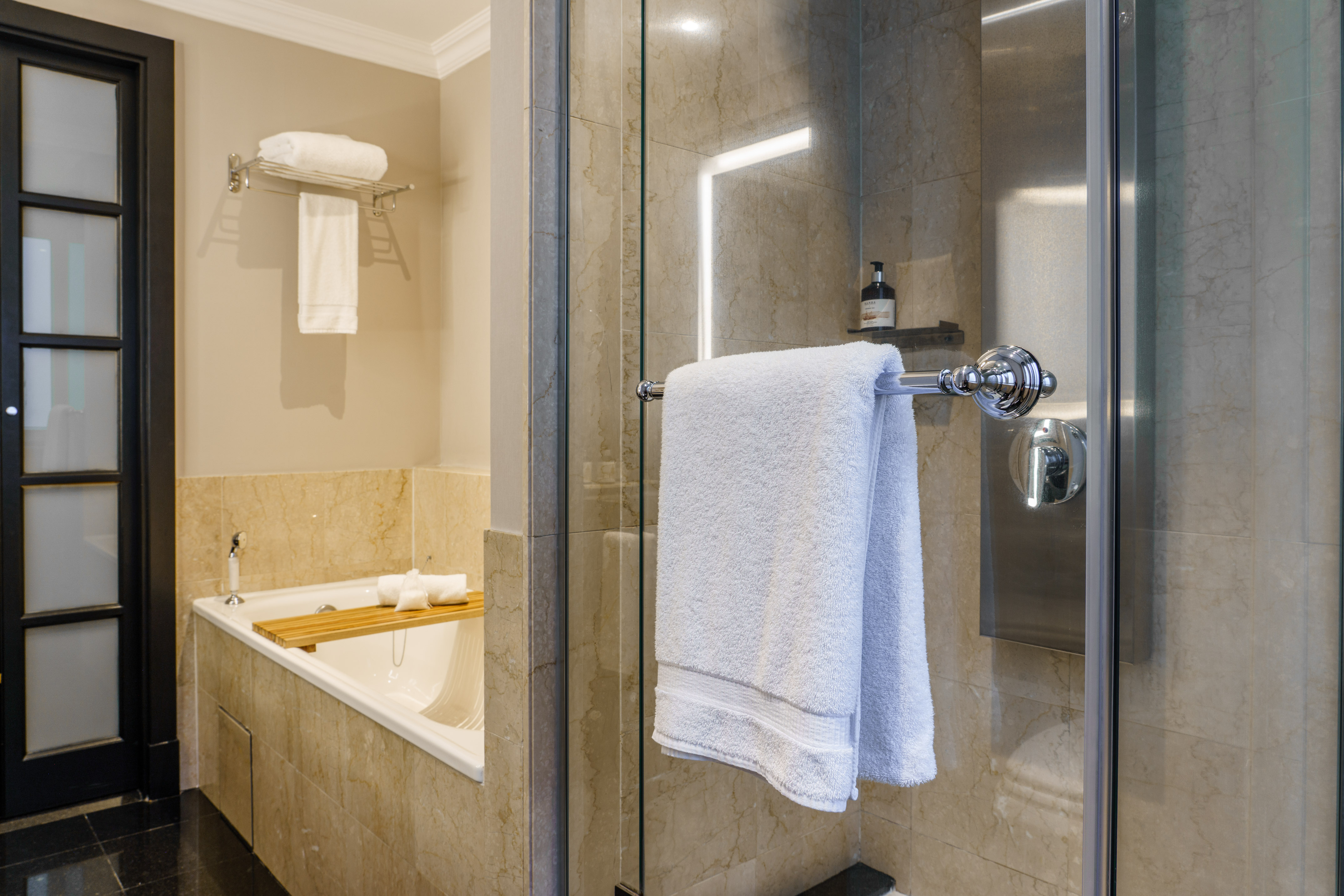 Modern bathroom with bathtub, glass shower, marble walls, and white towels.
