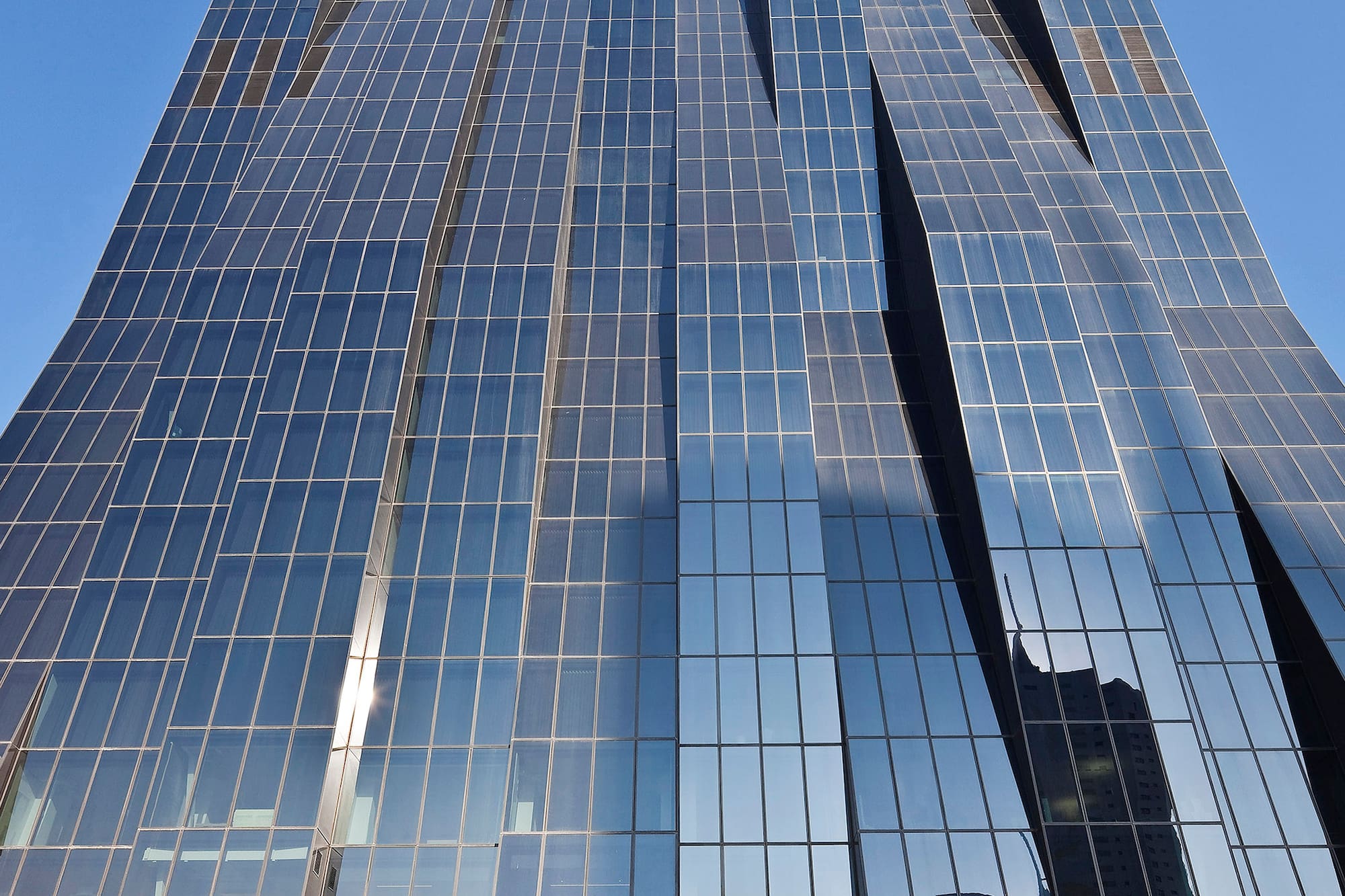 Modern undulating glass skyscraper facade reflecting blue sky.