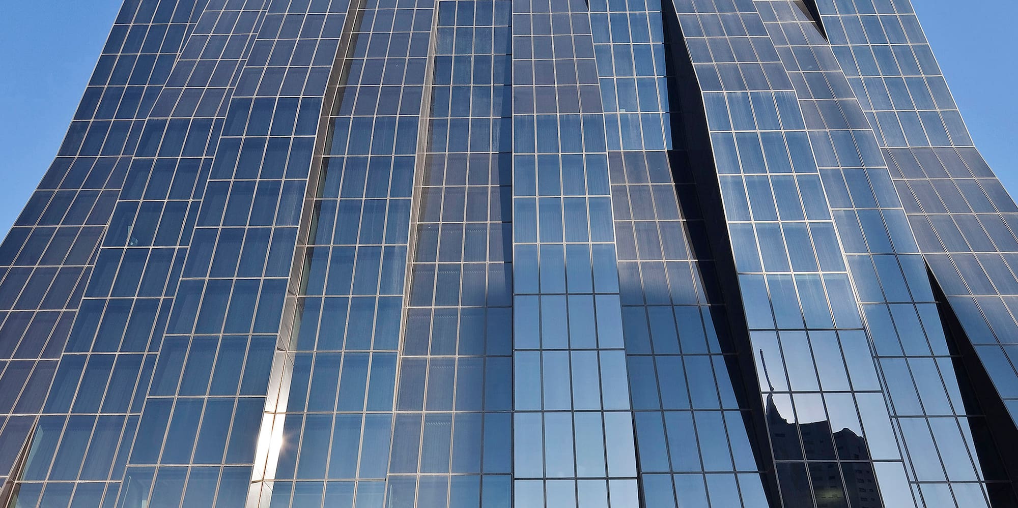 Modern skyscraper with wavy glass facade reflecting blue sky.