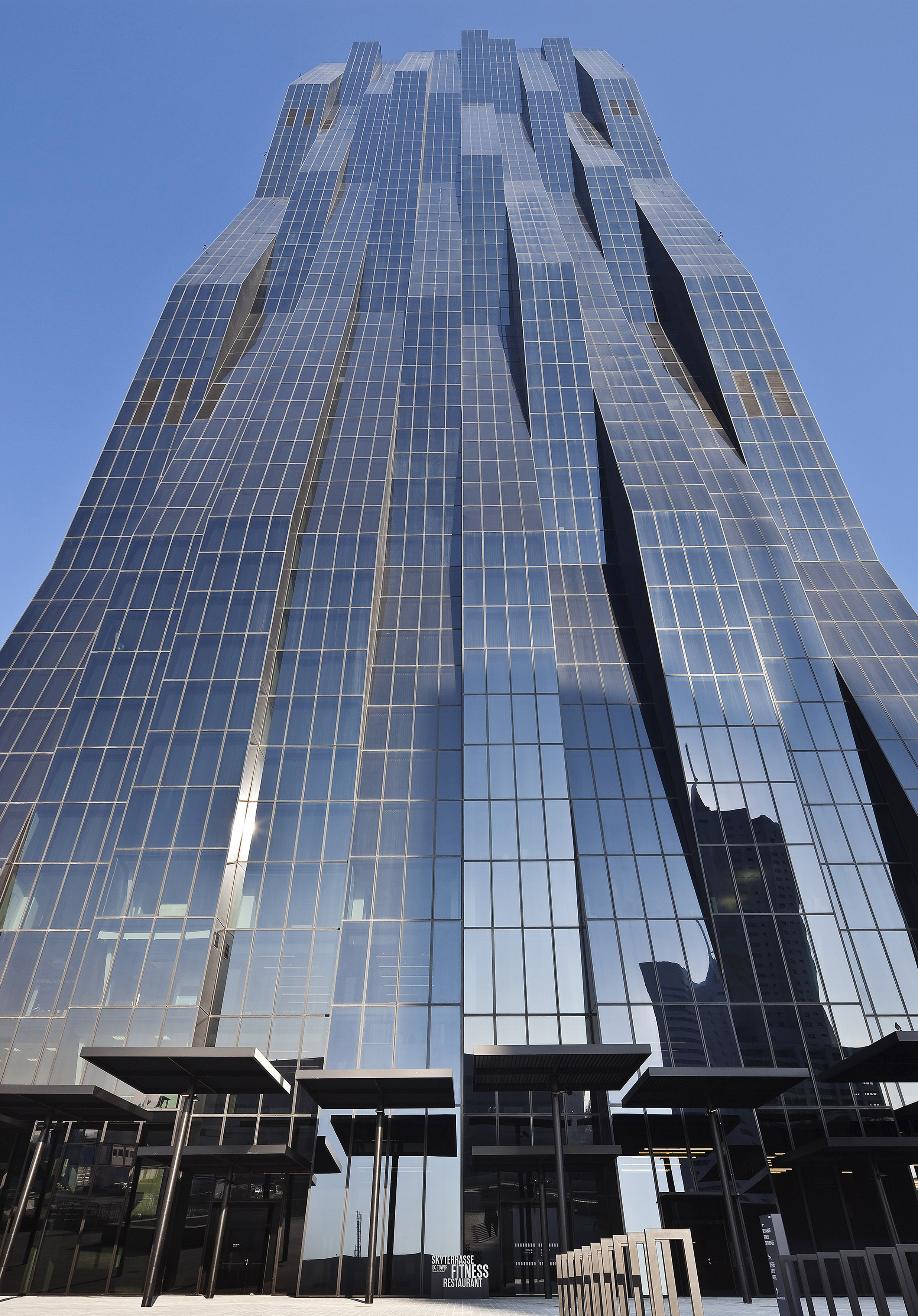 Modern skyscraper with wavy glass facade reflecting blue sky.