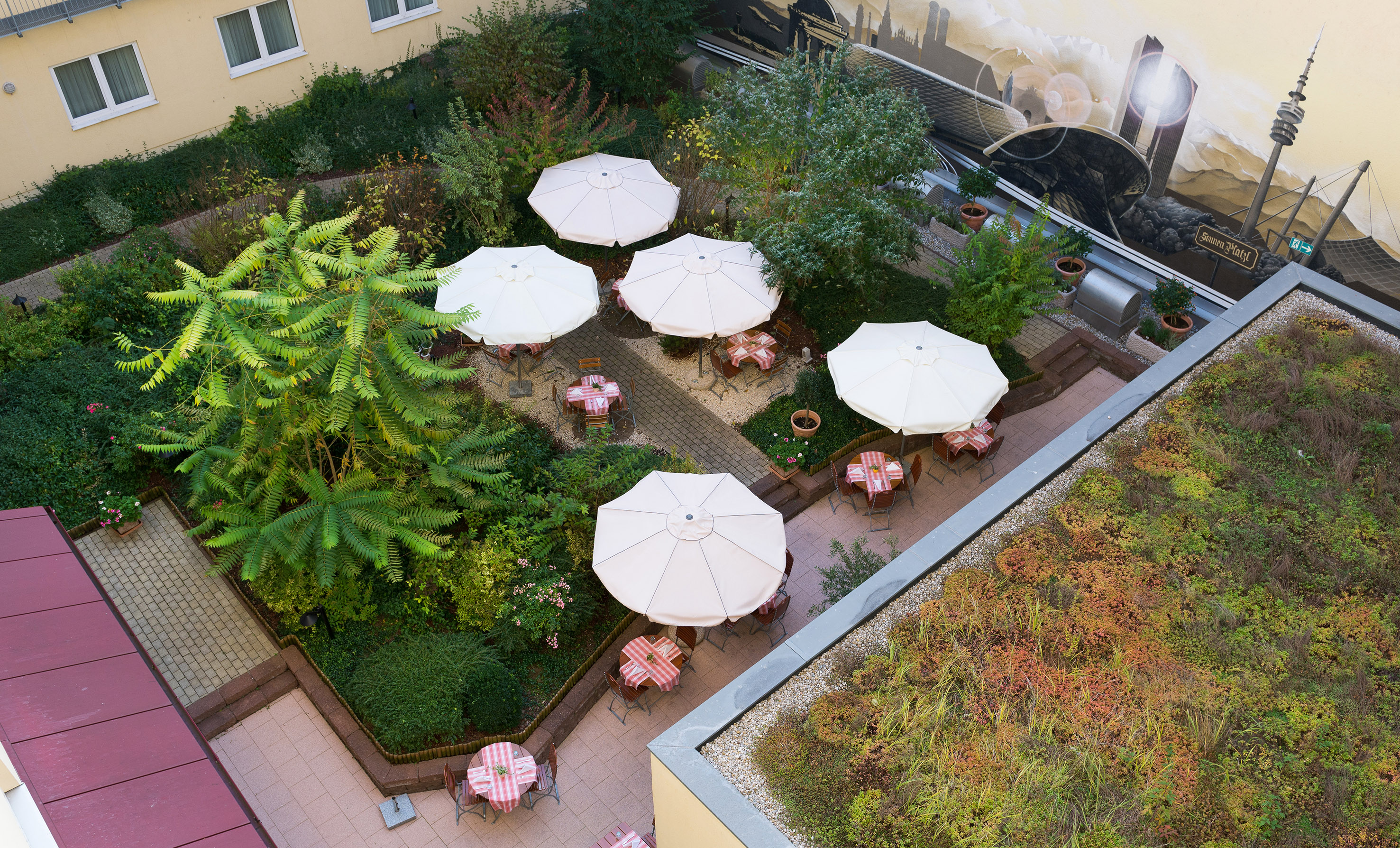 Hotel courtyard garden with outdoor cafe seating, white umbrellas, and green roof.