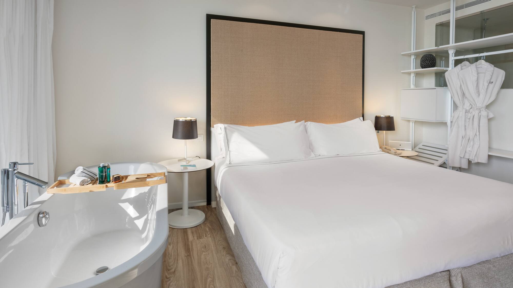 Luxury hotel bedroom with bed, freestanding tub, and bathrobes.