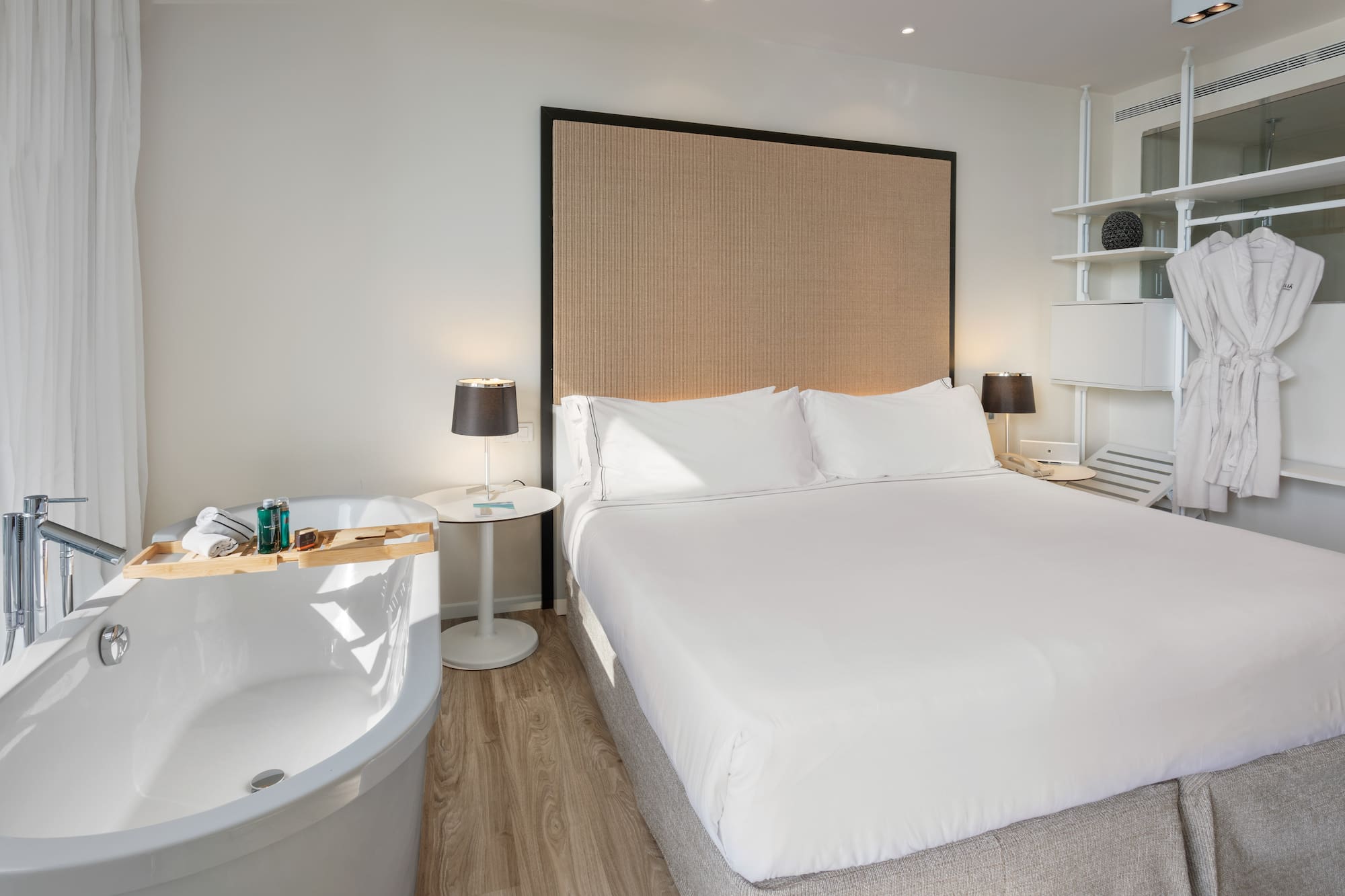 Luxury hotel bedroom with bed, freestanding tub, and bathrobes.