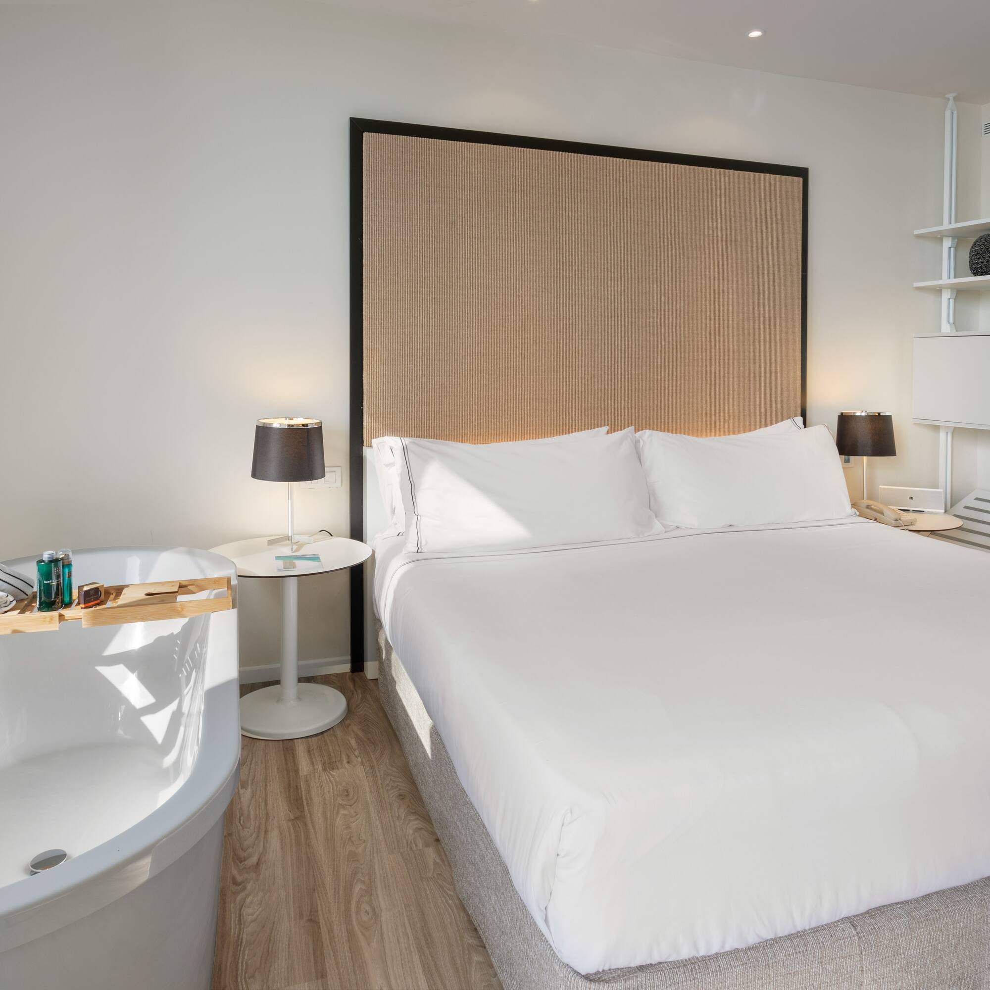 Luxury hotel bedroom with bed, freestanding tub, and bathrobes.