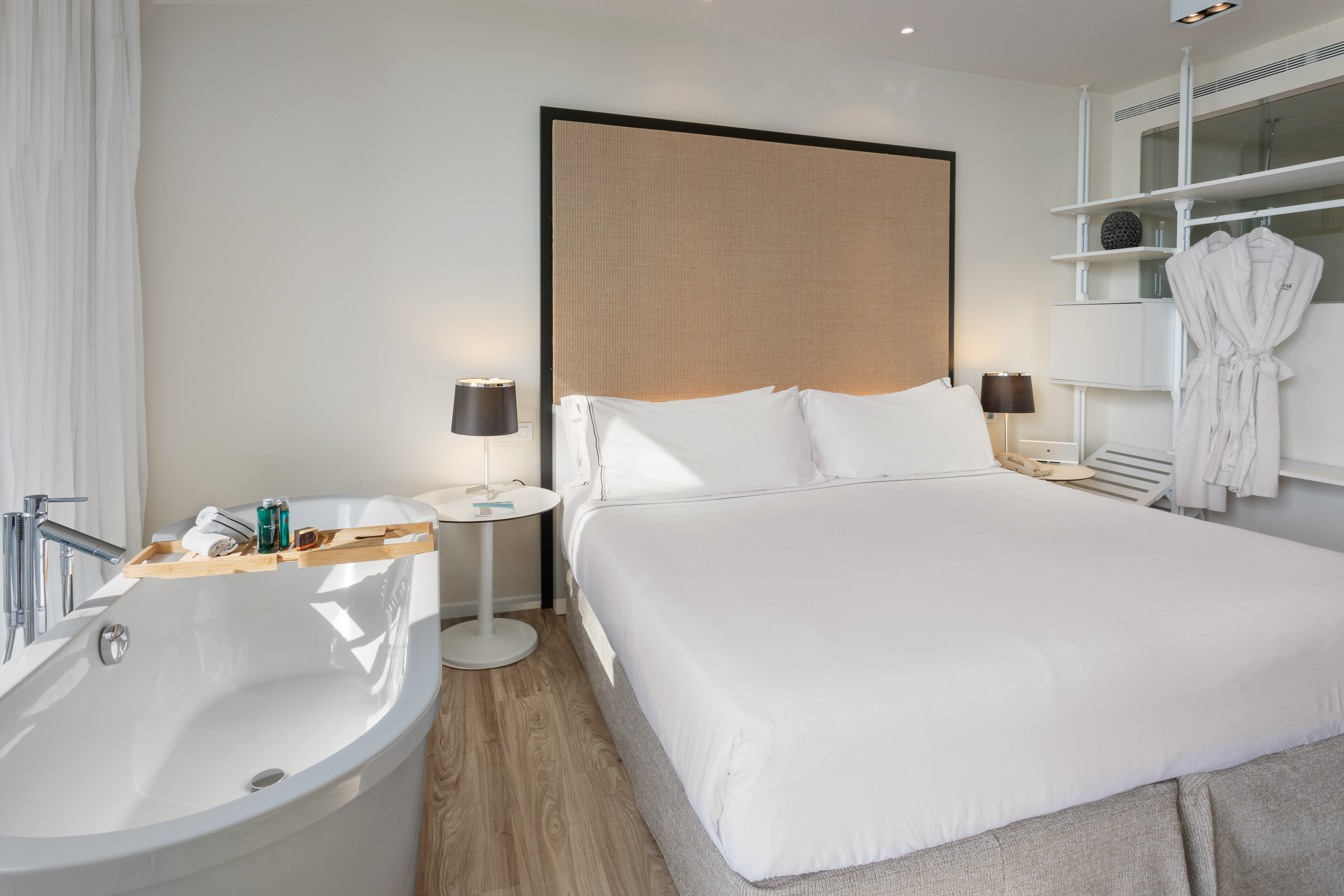 Luxury hotel bedroom with bed, freestanding tub, and bathrobes.