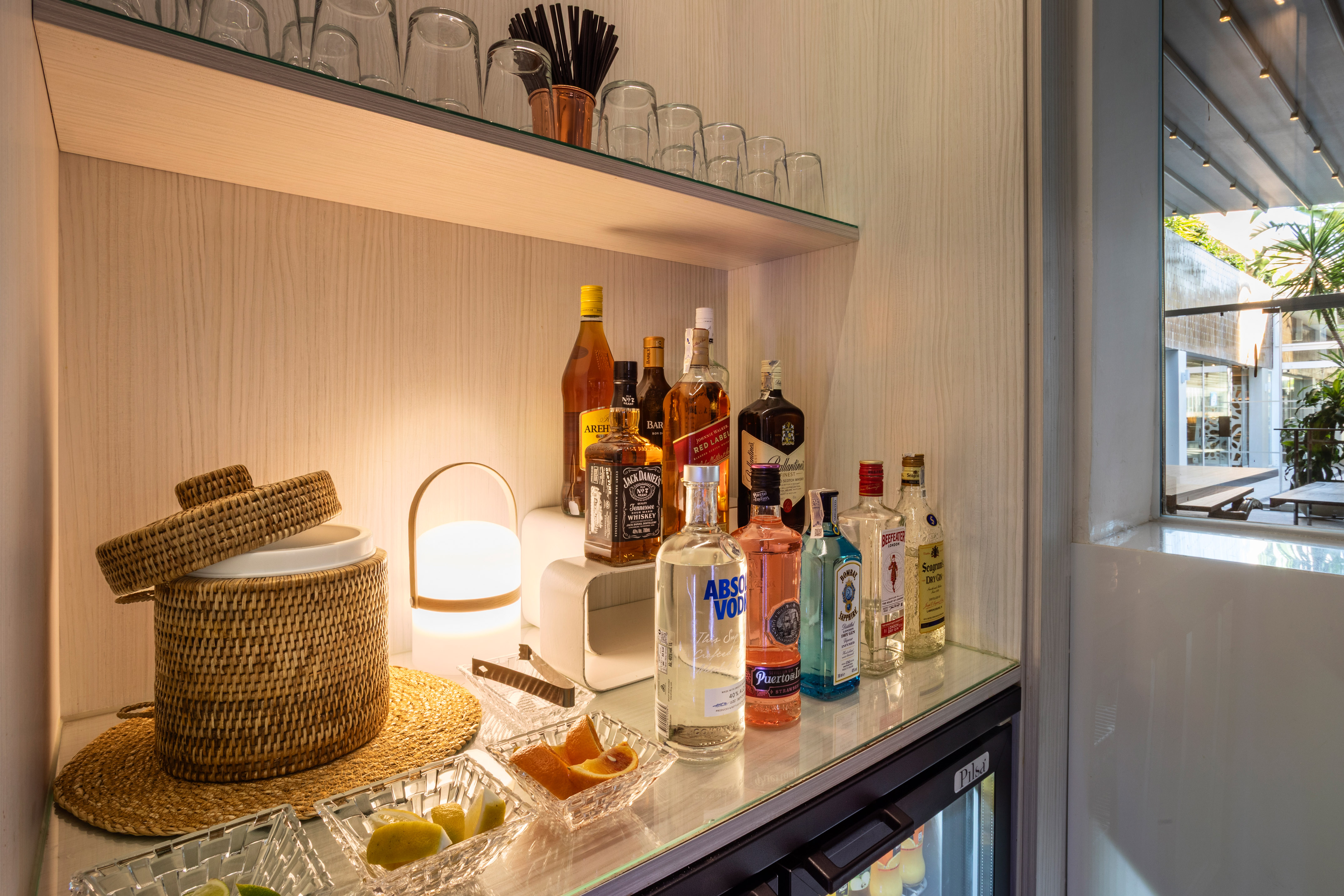 Minibar with various liquor bottles, cocktail garnishes, glassware, and lamp.