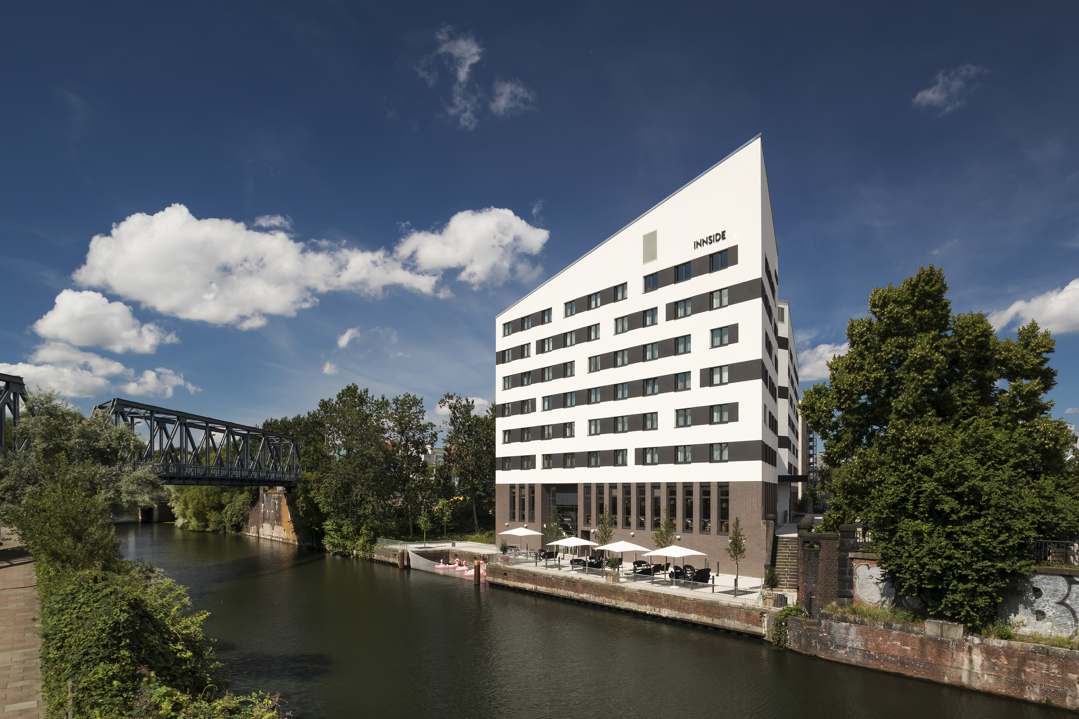 Angular INNSIDE hotel by river, outdoor patio, and metal bridge.