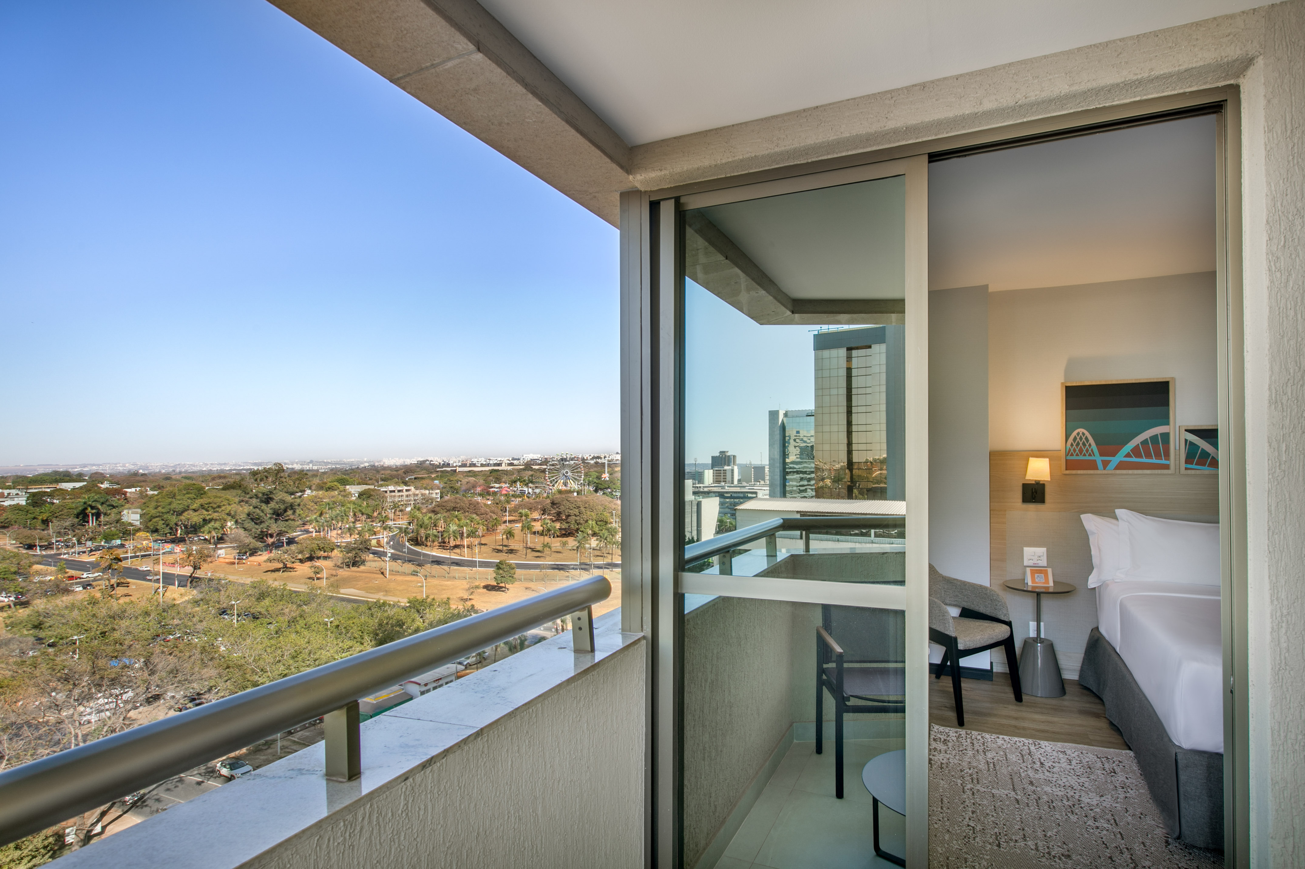 Balcony view from hotel room, showing city, green areas, and modern bedroom.