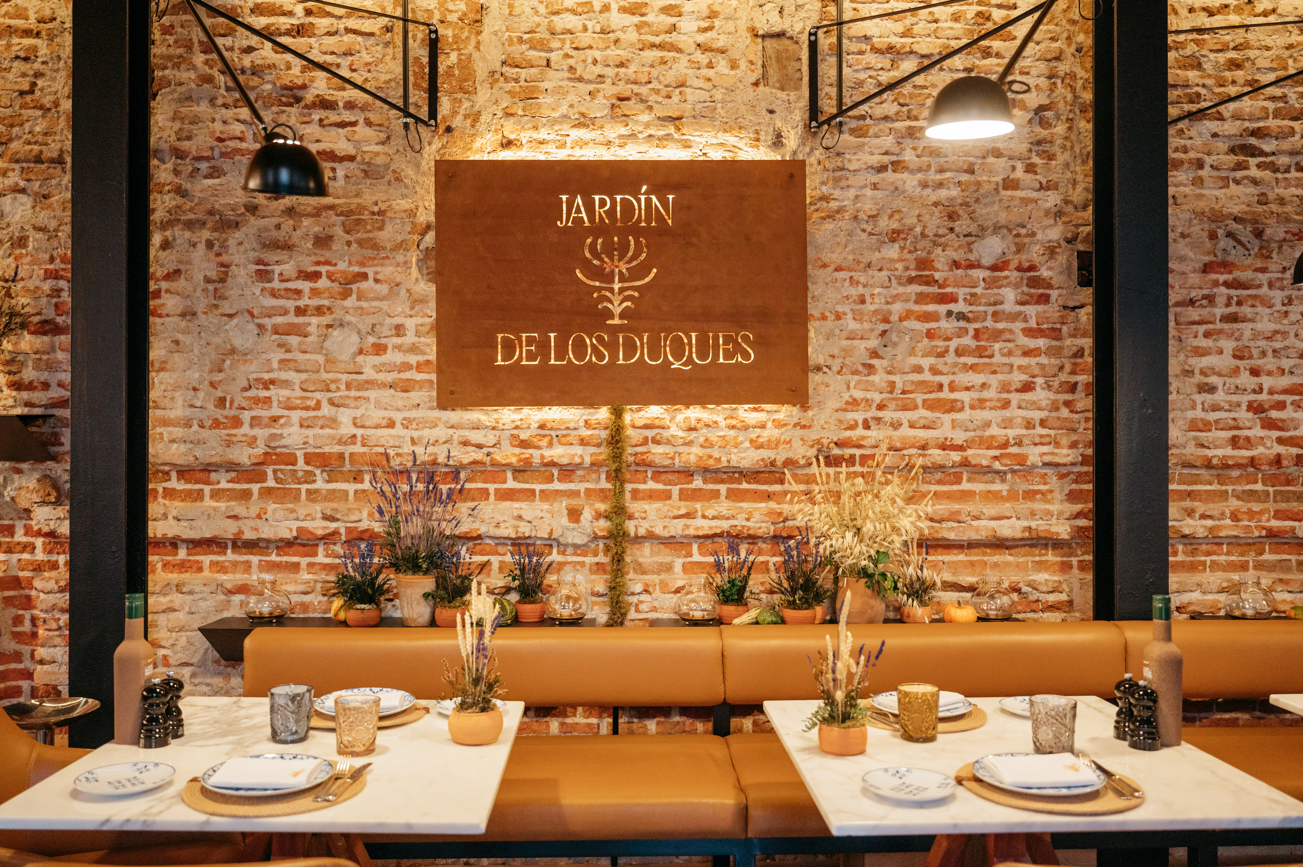 JARDÍN DE LOS DUQUES restaurant interior: brick wall, leather booths, modern decor.