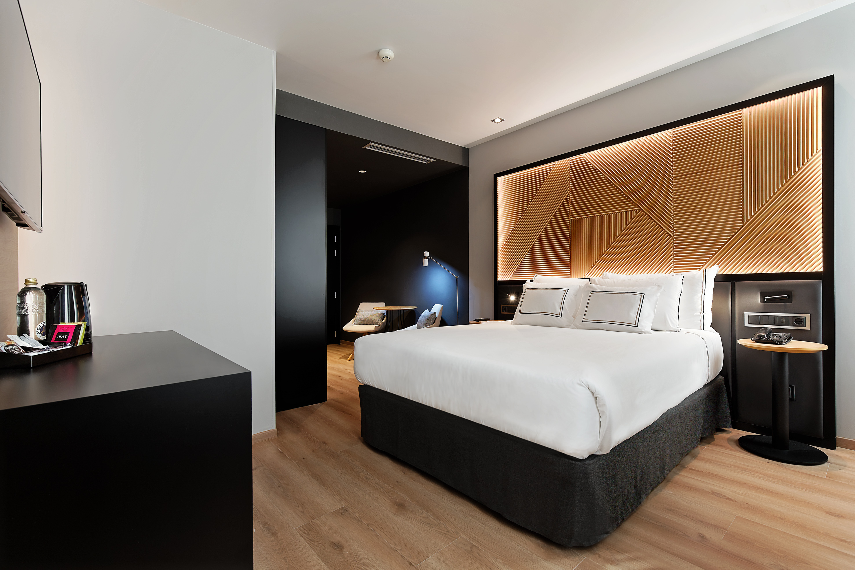 Modern hotel room with king bed, geometric wood headboard, and stylish design.